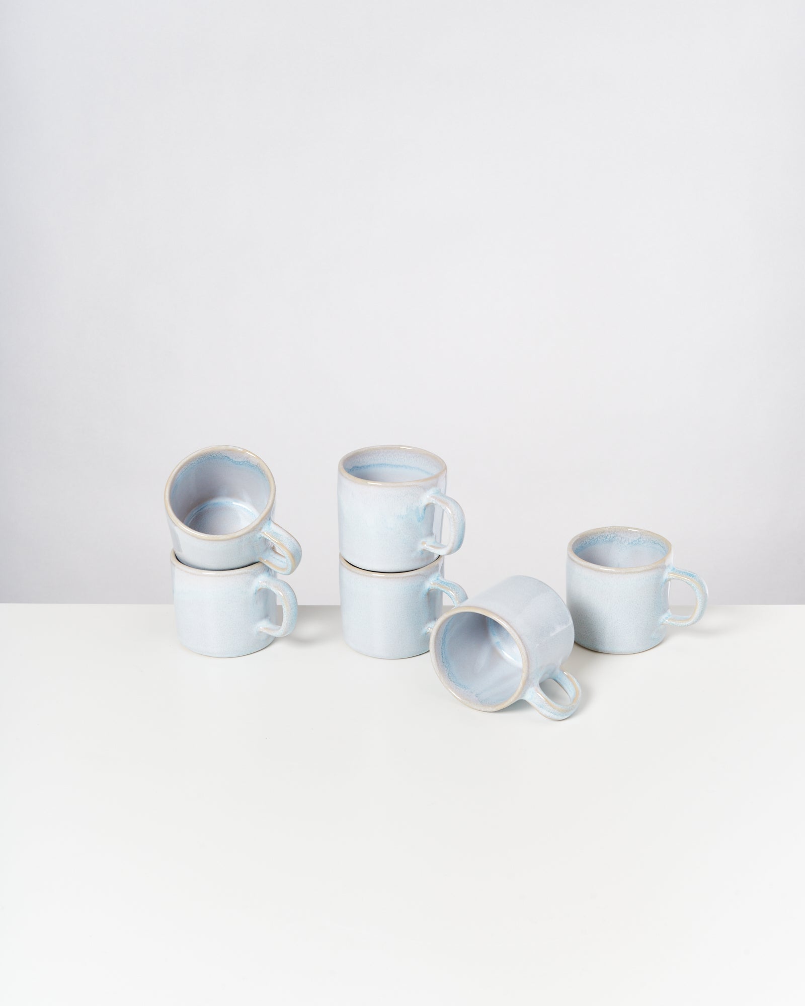 Sechs blaue Keramiktassen, einige gestapelt, stehen auf einem weißen Tisch.