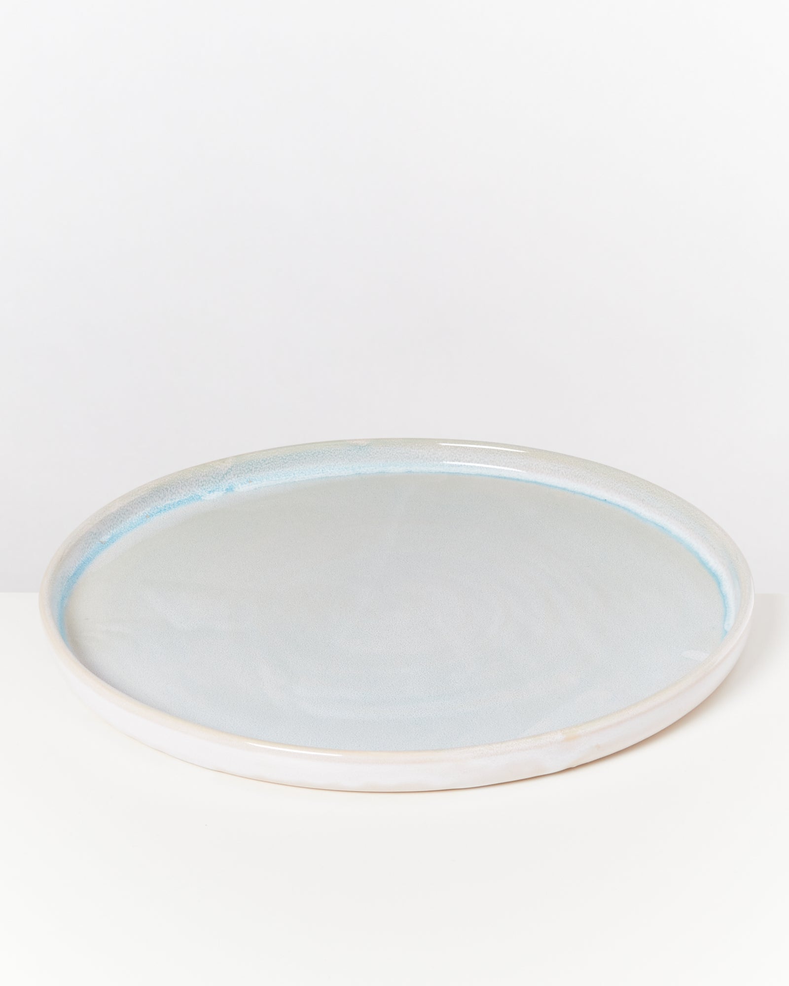 Weißer, runder Keramikteller mit bläulichem Rand auf einem hellen Hintergrund.