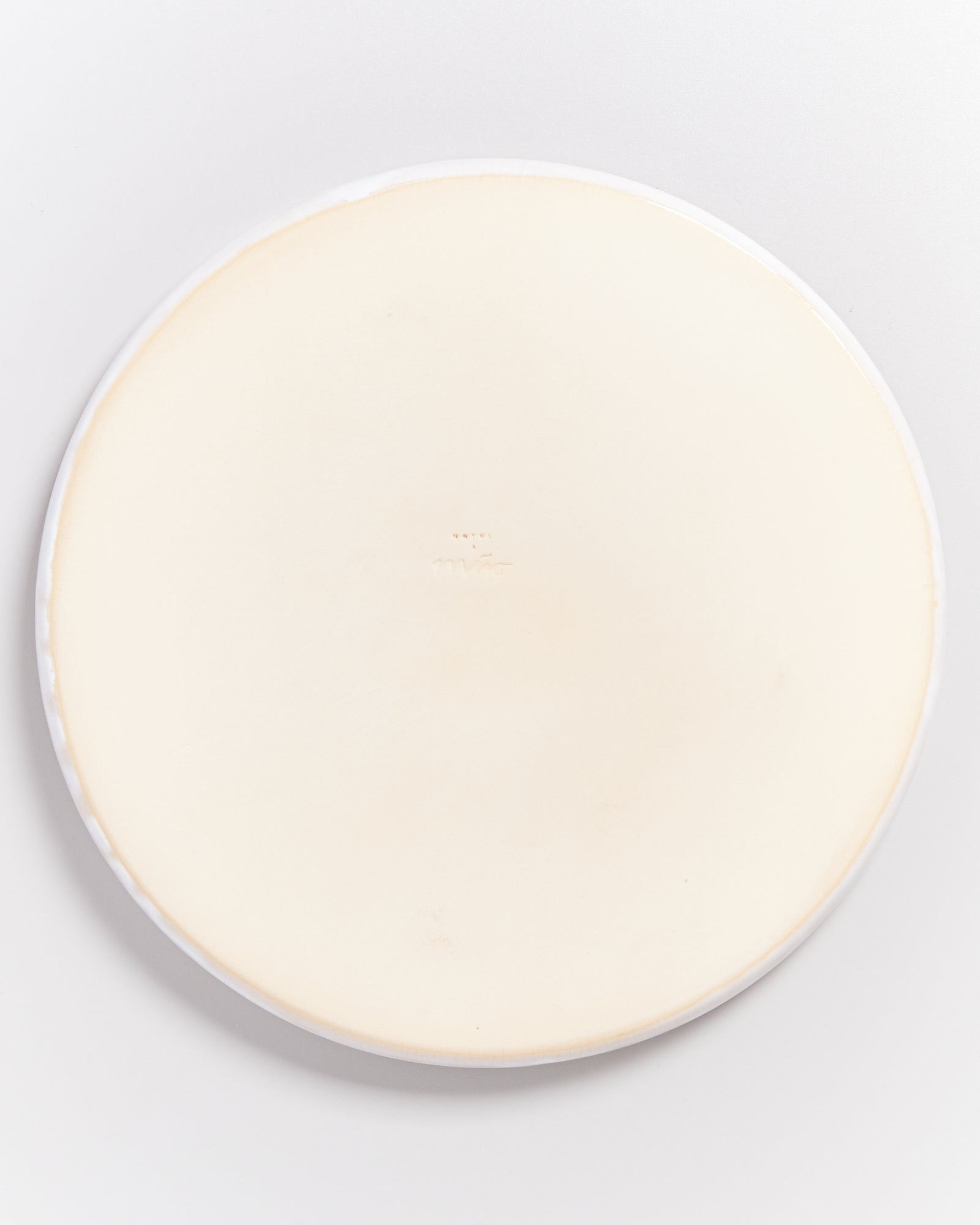 Rückseite eines hellen, runden Tellers mit einem kleinen, mittigen Logo.