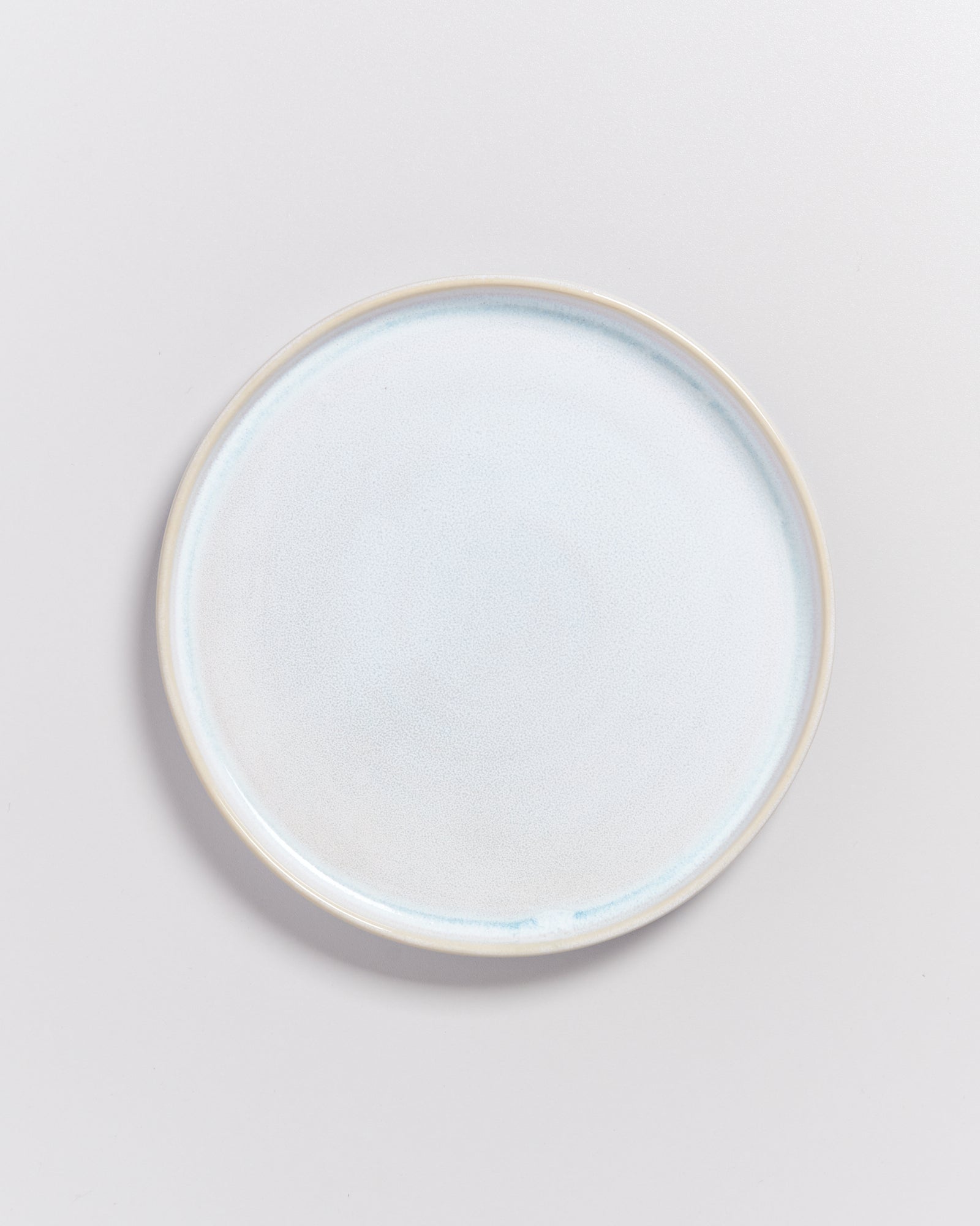 Ein heller, runder Keramikteller mit leicht bläulichem Schimmer auf einem hellen Hintergrund.