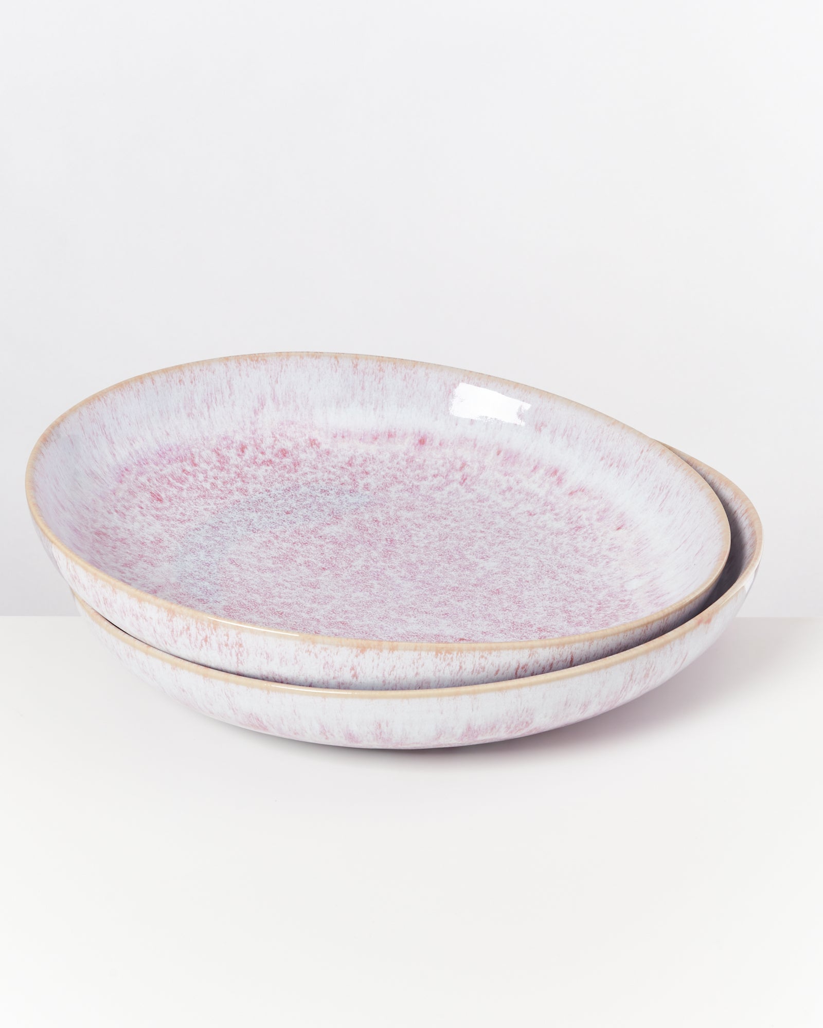 Zwei pastellrosa Schalen mit gesprenkeltem Muster stehen übereinander auf weißem Hintergrund.