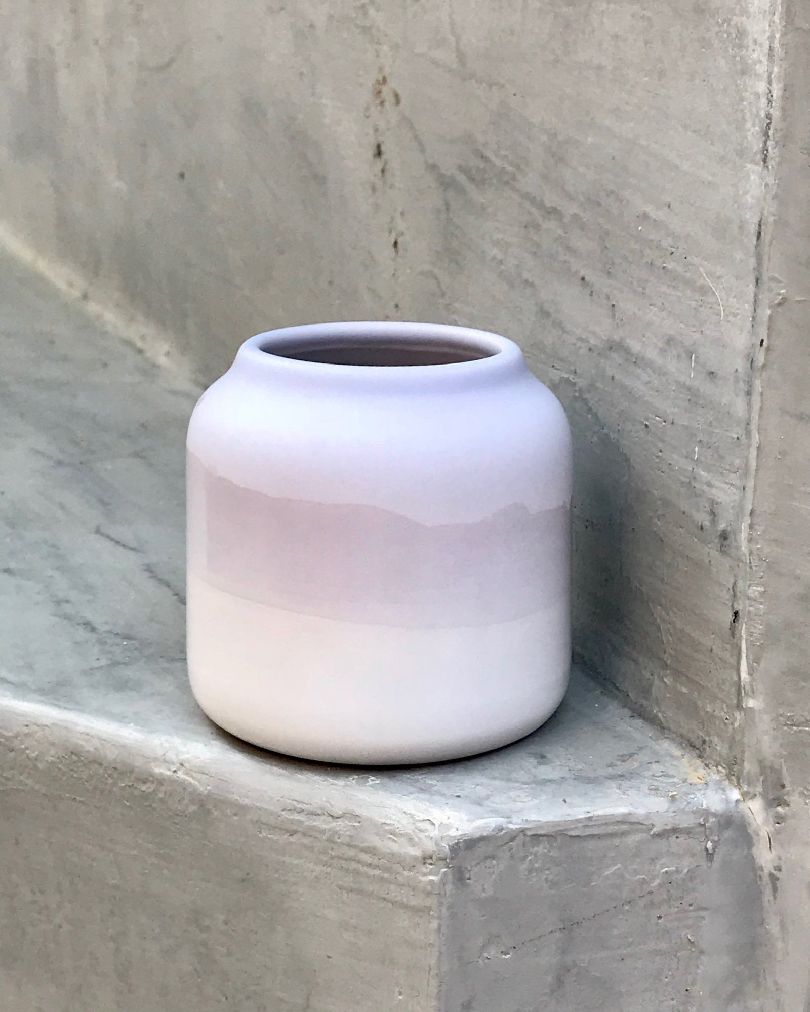 Ein cremefarbener Keramiktopf mit lila Streifen steht auf einer grauen Betonoberfläche.