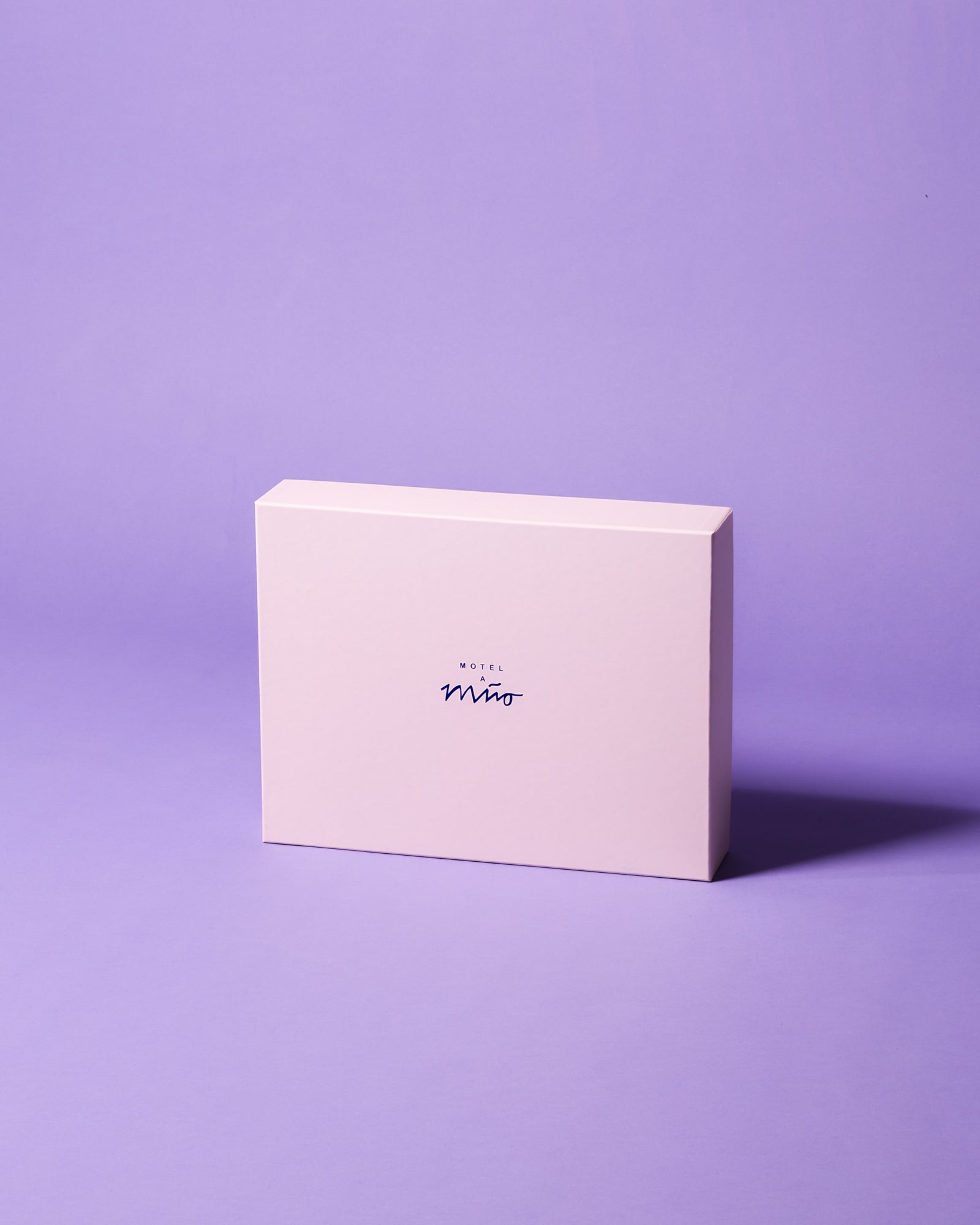 Eine hellrosa Schachtel mit der Aufschrift "Motel" steht vor einem lila Hintergrund.