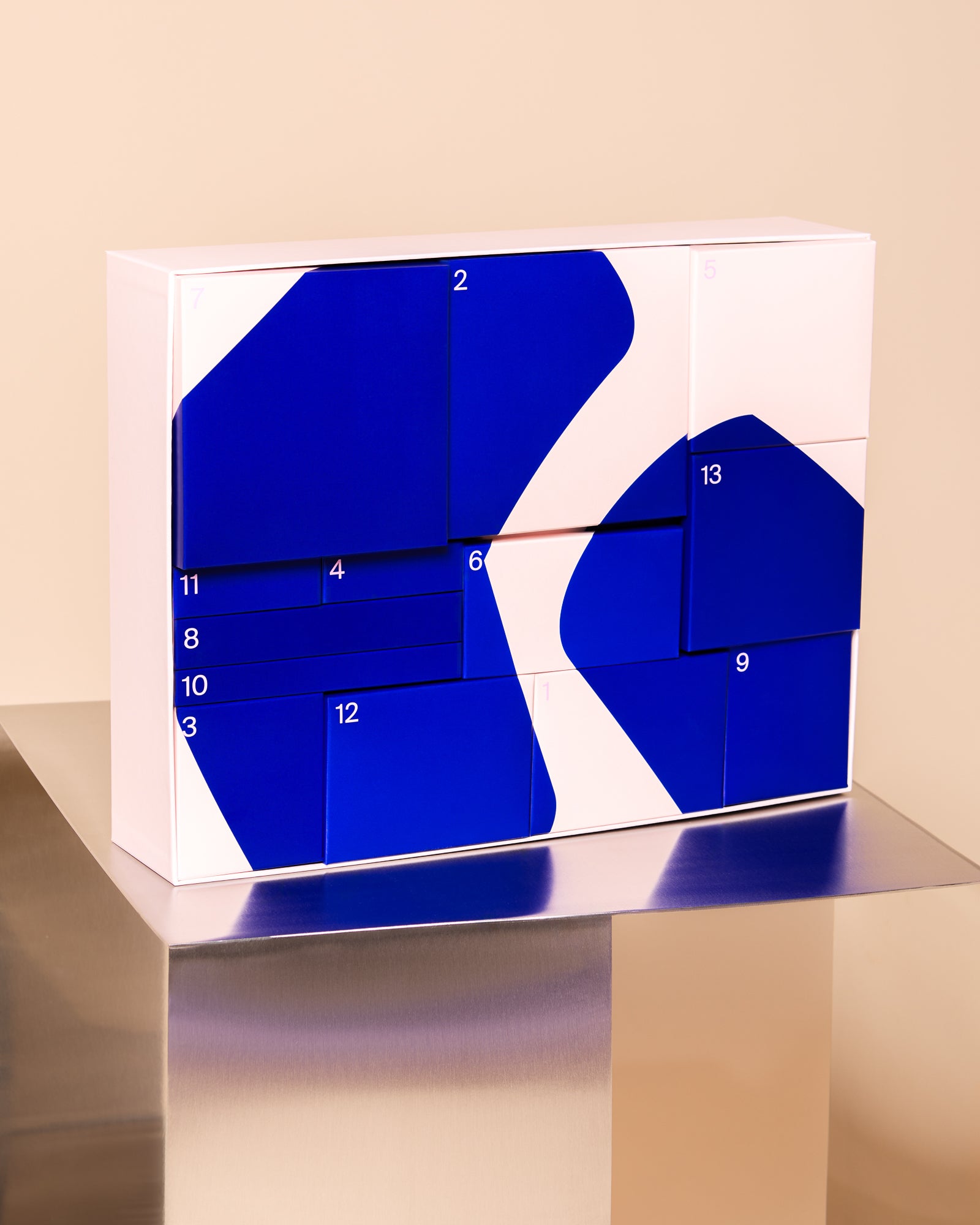 Blauer und weißer Adventskalender auf einem metallischen Tisch vor beigem Hintergrund.