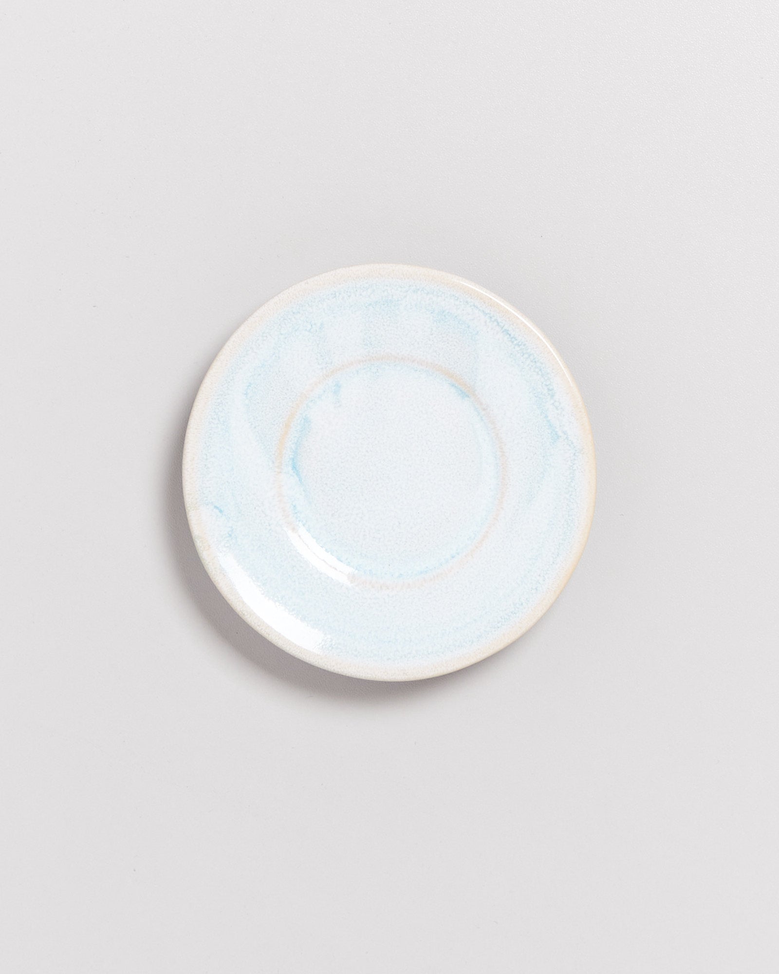 Kleiner weißer Teller mit blauen Akzenten auf hellgrauem Hintergrund abgebildet.