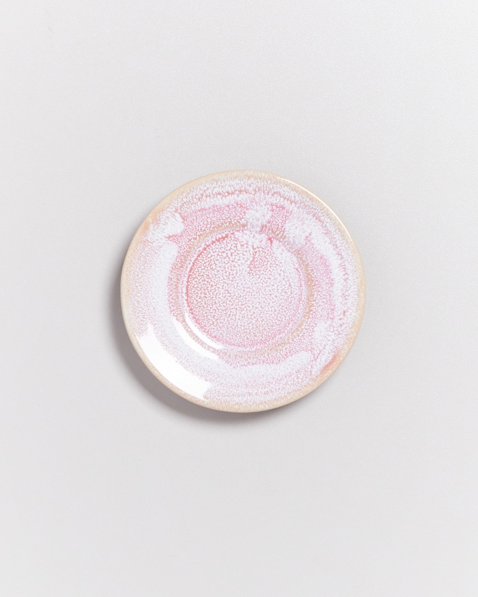 Runder Teller mit rosa und weißen Mustern auf einer neutralen, hellen Oberfläche.