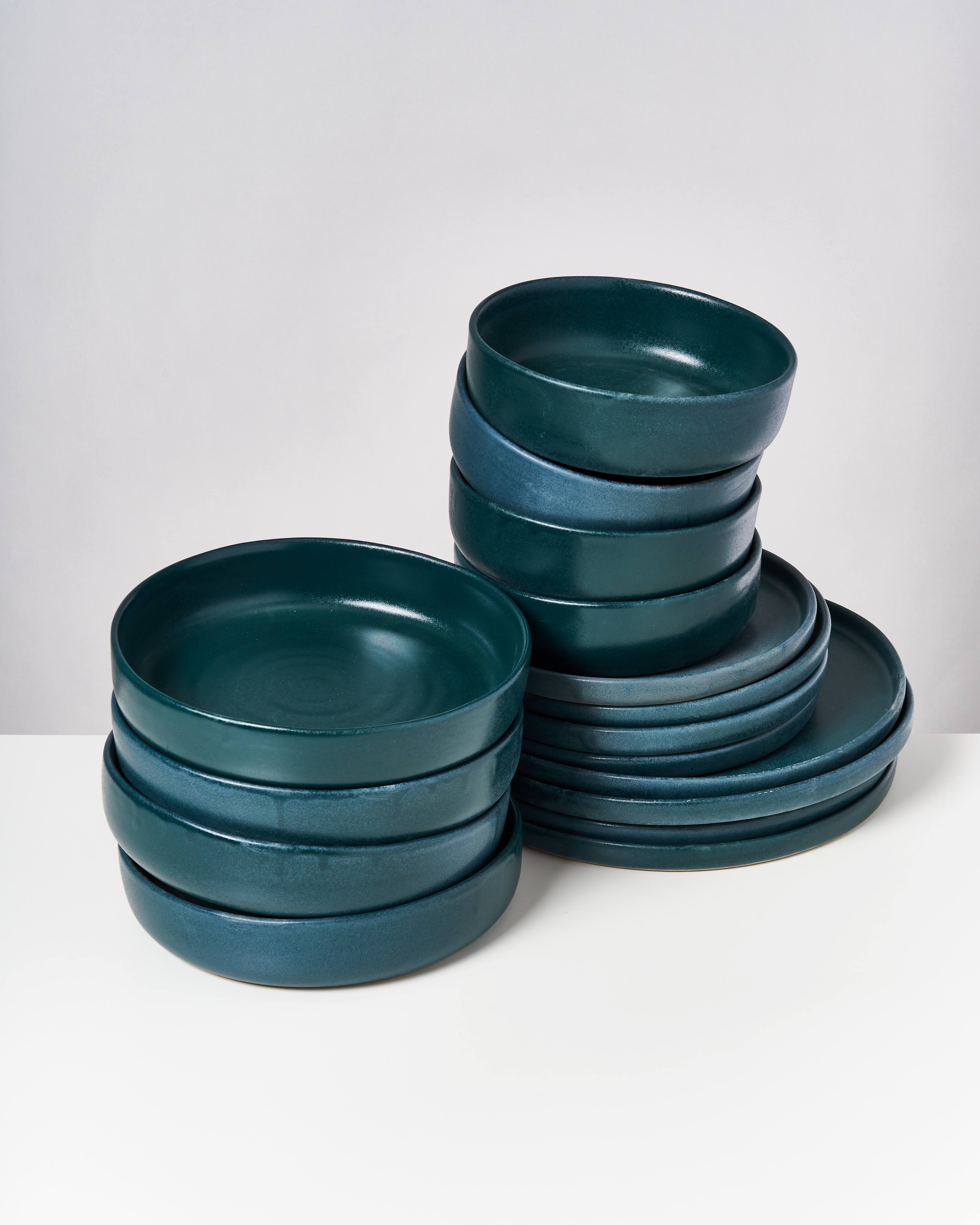 Ein Stapel türkisfarbener Keramikteller steht auf einem weißen Tisch vor einem neutralen Hintergrund.