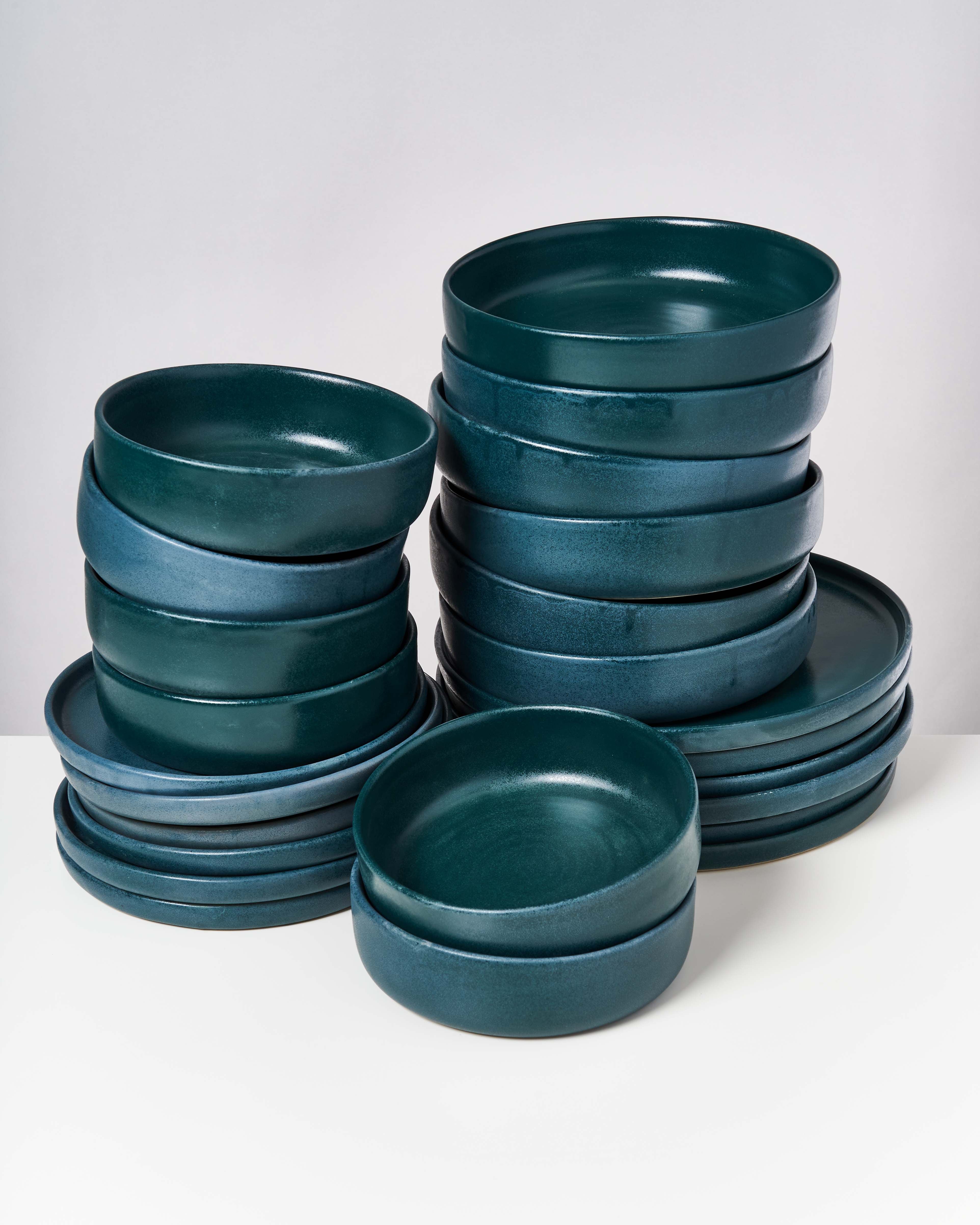 Ein Stapel mit dunkelgrünen, modernen Keramiktellern und Schalen auf weißem Hintergrund.