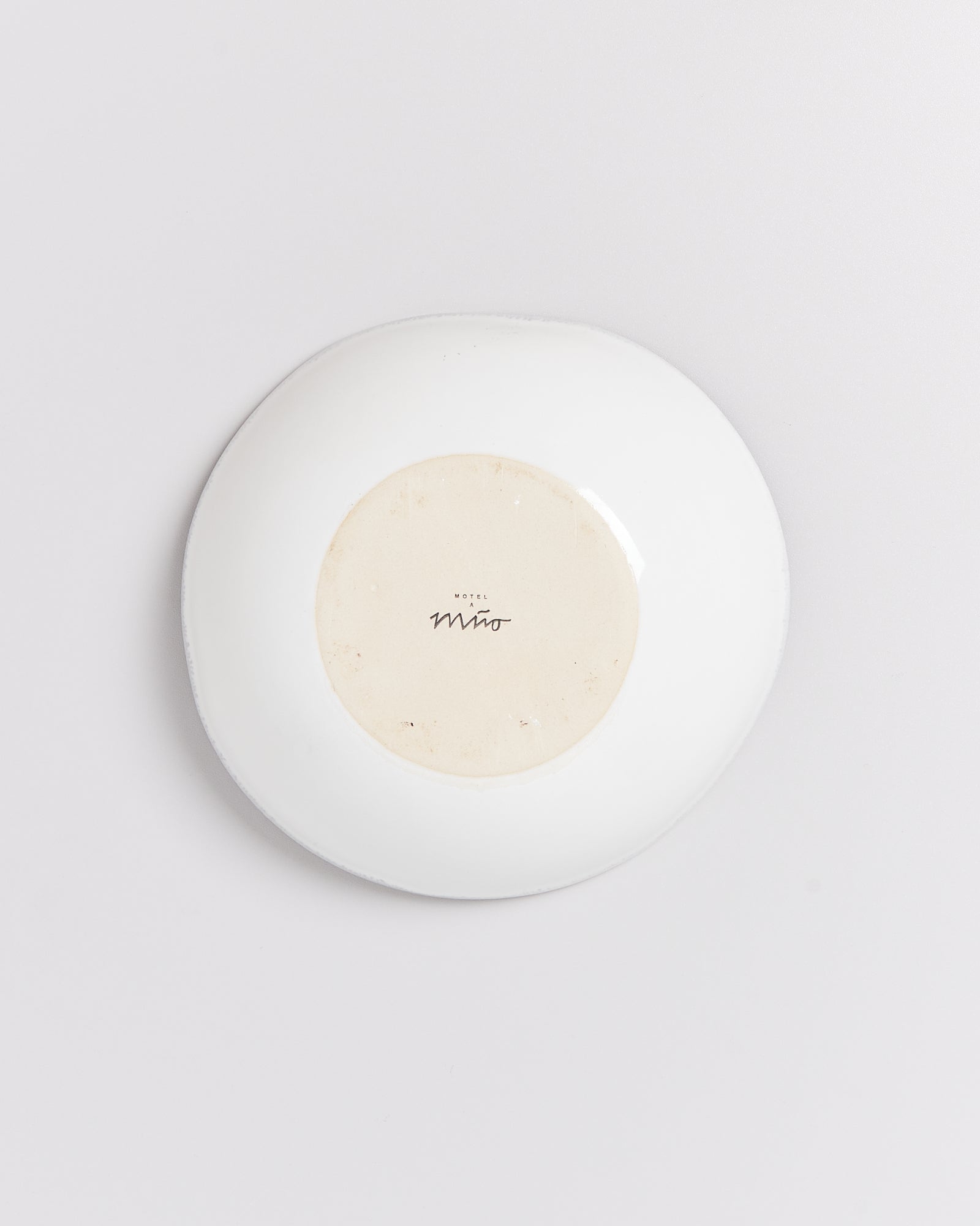 Weiße Schale mit einem Etikett am Boden, das "MODEL M" und eine Signatur zeigt, auf grauem Hintergrund.