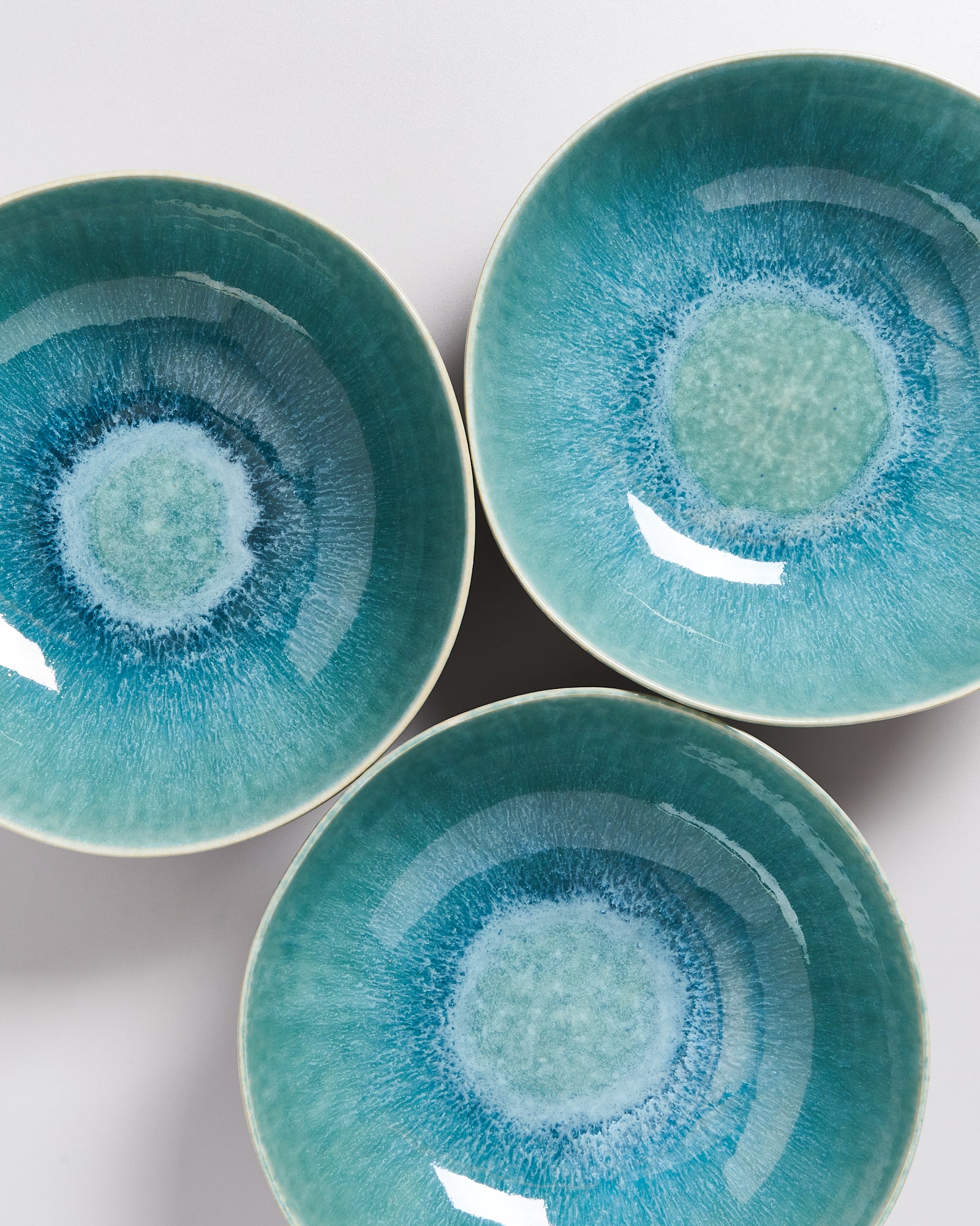Drei türkisfarbene Keramikteller mit kreisförmigem Muster liegen auf einer hellen Oberfläche.