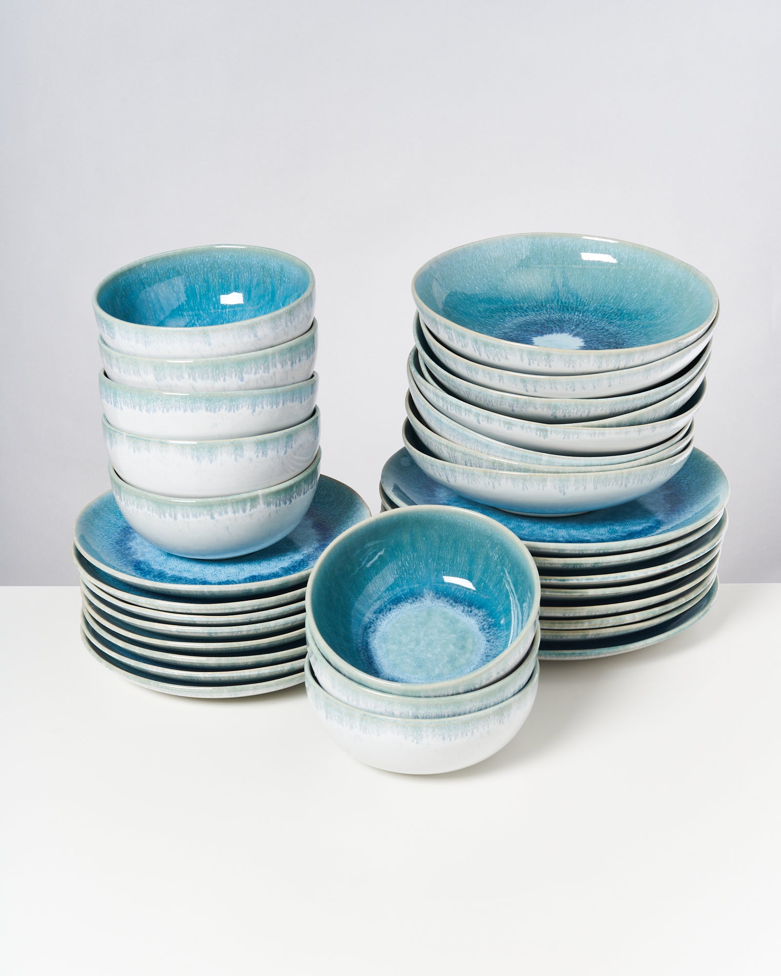 Gestapelte, blau-weiße Keramikschalen und Teller auf einem weißen Tisch.