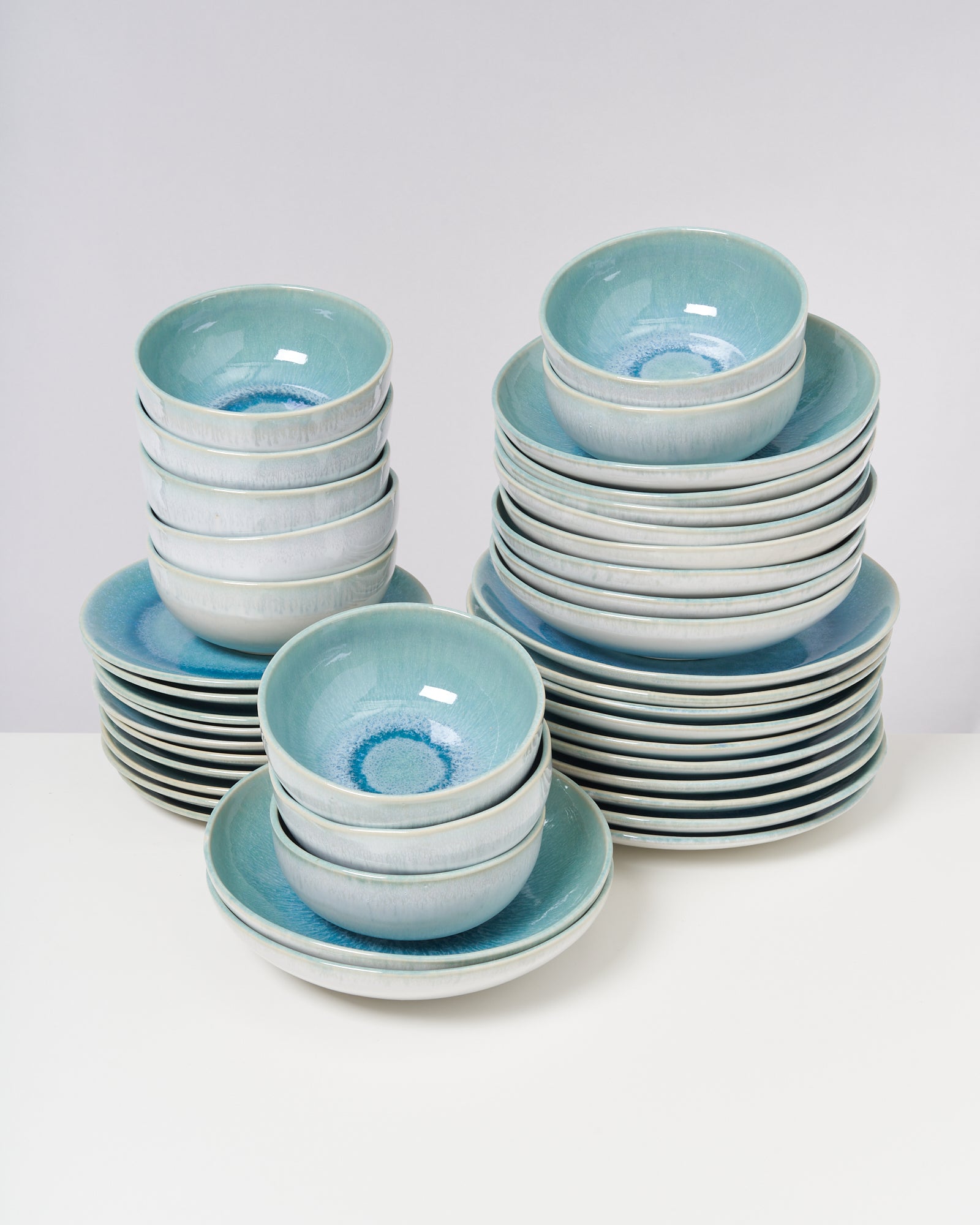 Mehrere Stapel von türkisen Keramikschüsseln und -tellern auf einem weißen Tisch.