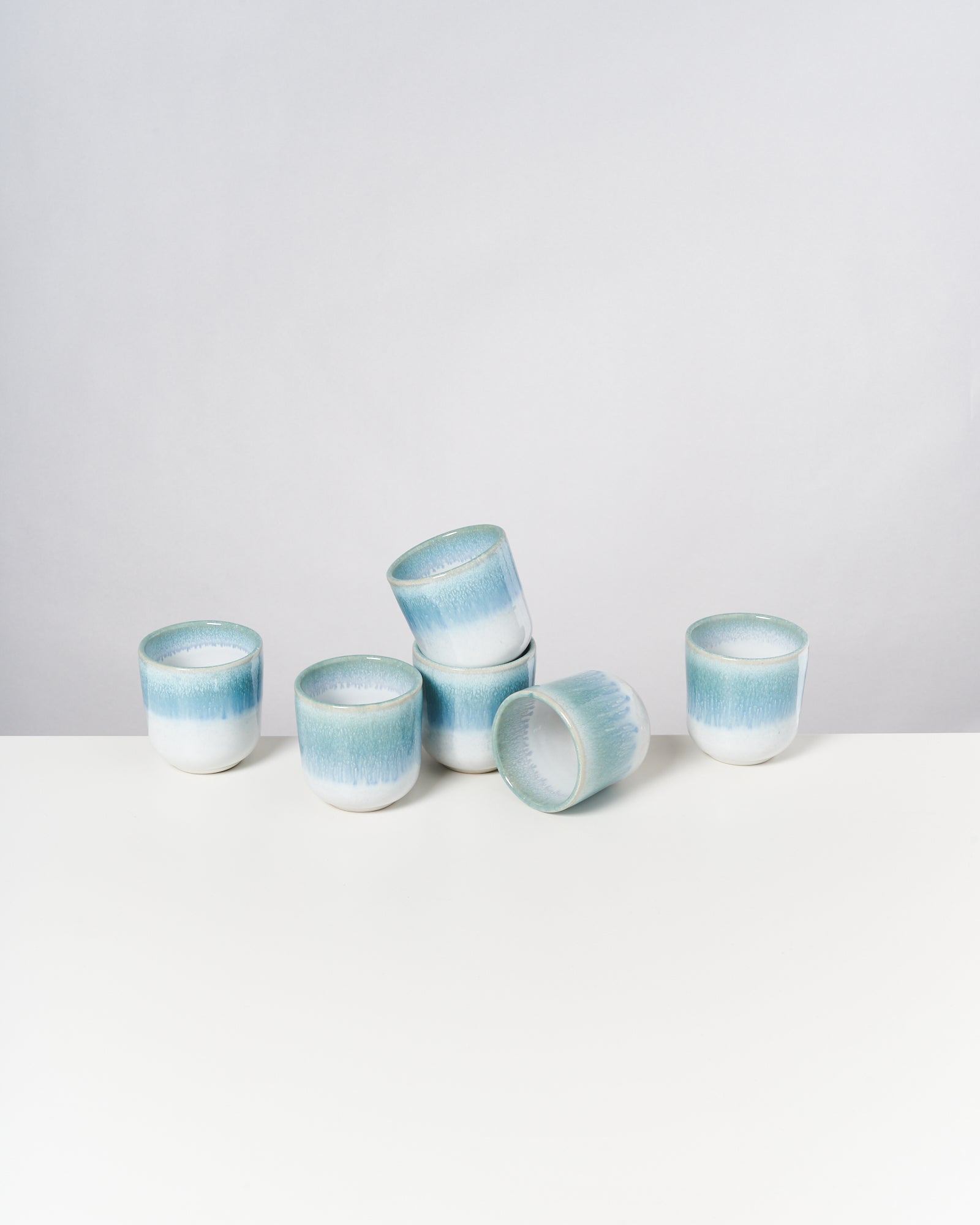 Sechs blau-weiße Tassen auf einem weißen Tisch, vier stehen, zwei sind gestapelt.