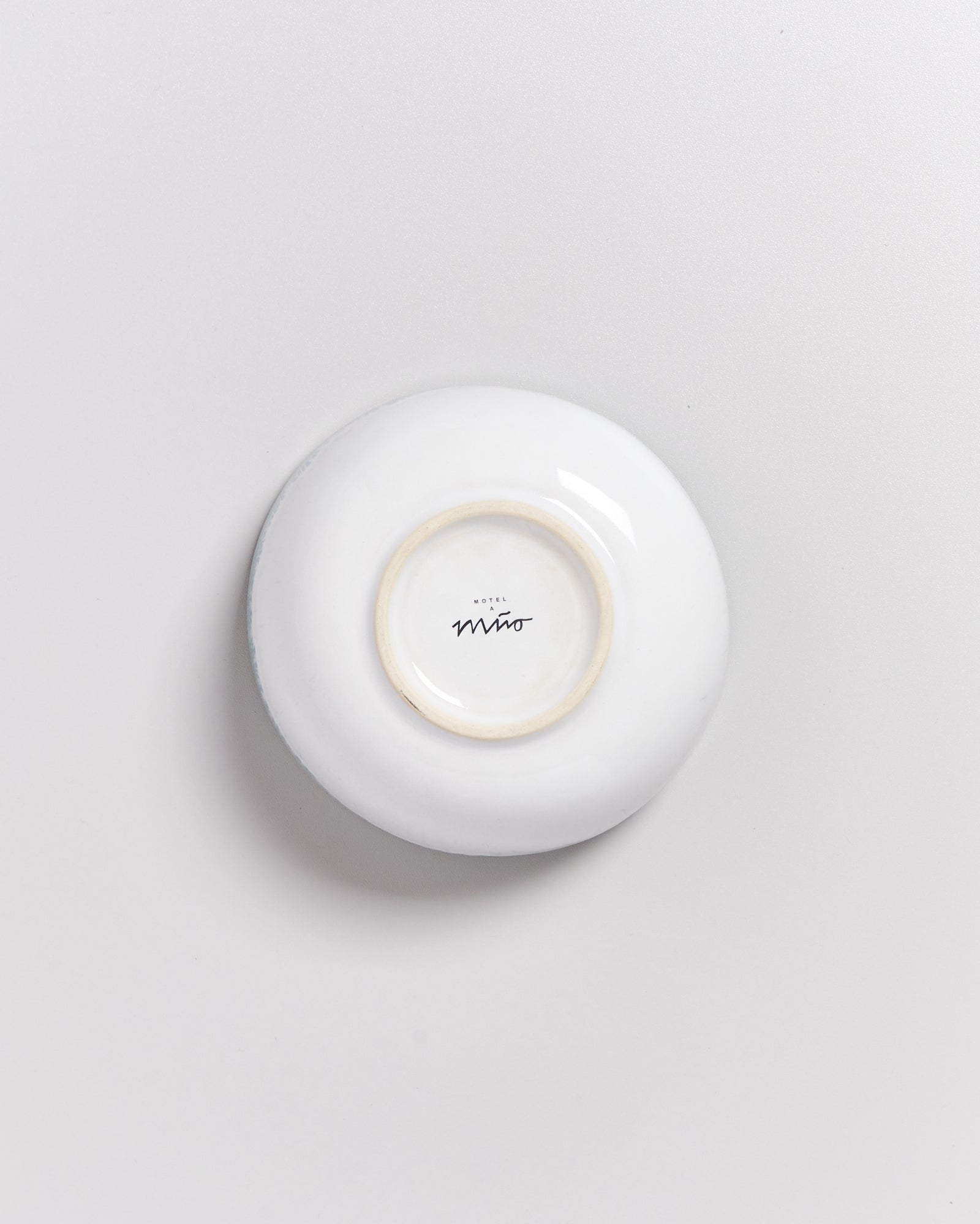Weiße Unterseite einer Tasse mit dem Schriftzug "Hotel Miro" auf einem hellgrauen Hintergrund.