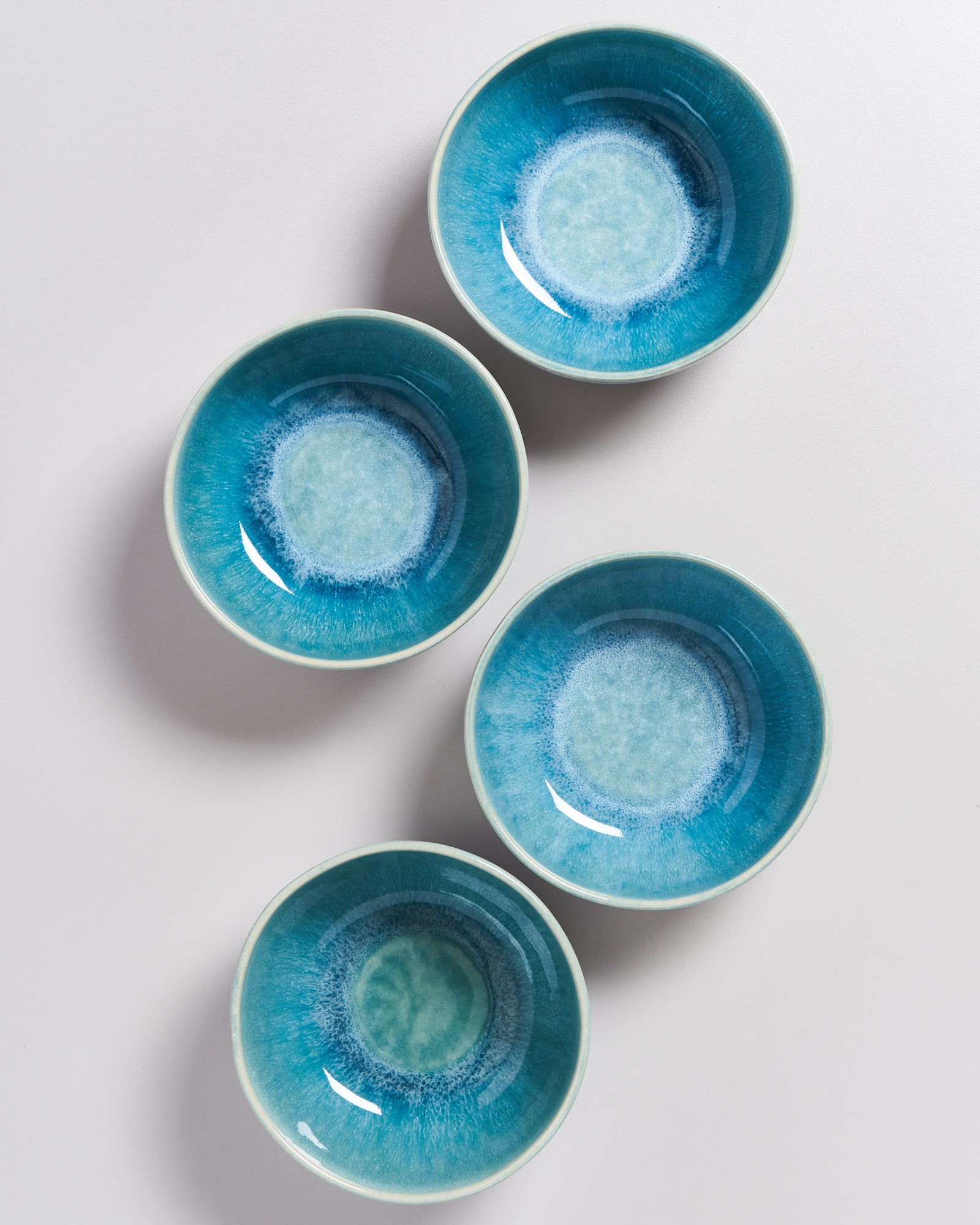 Vier türkisblaue Schalen mit blauen und weißen Kreismustern auf hellgrauem Hintergrund arrangiert.
