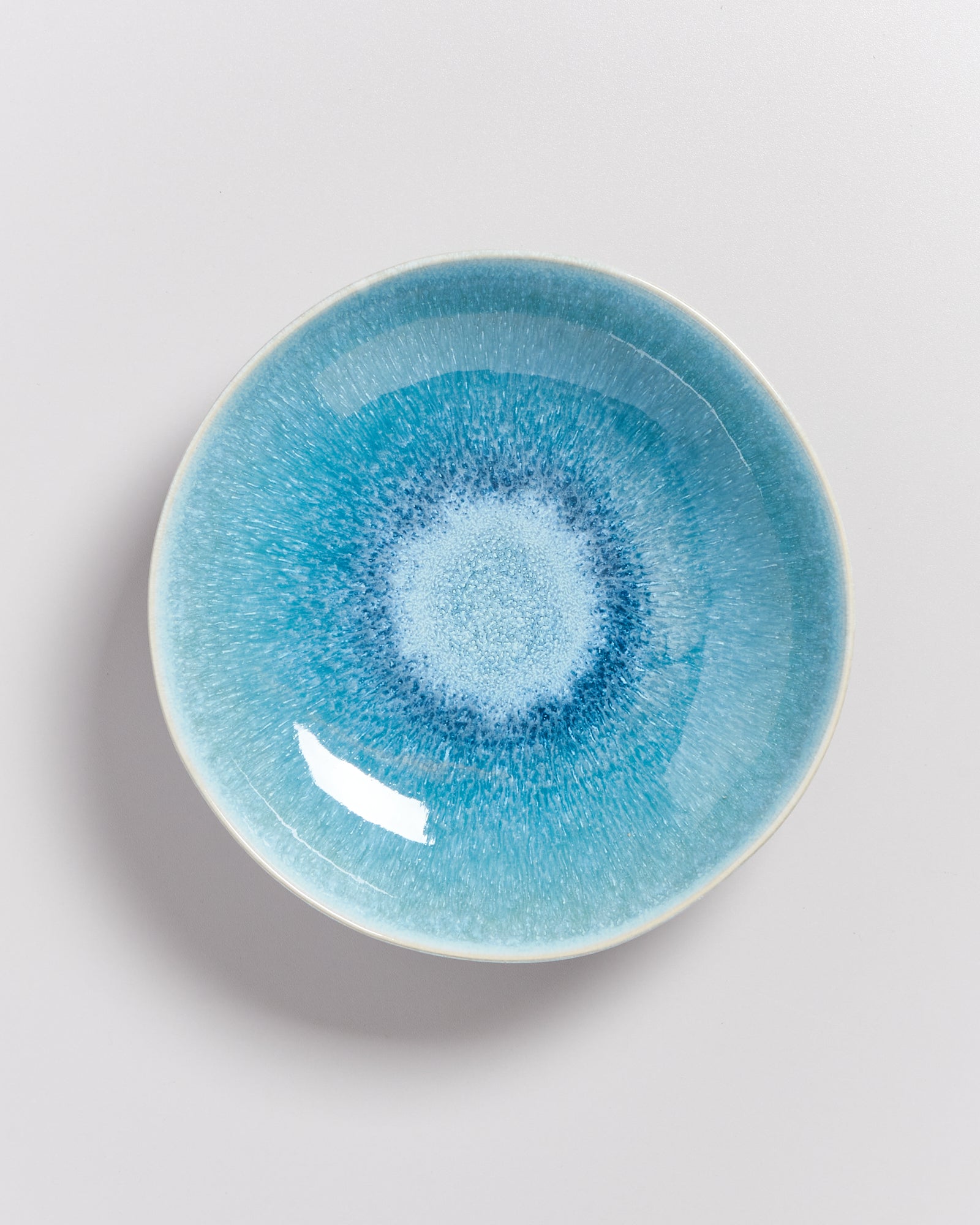 Blauer, runder Teller mit einem weißen, gesprenkelten Muster in der Mitte auf weißem Hintergrund.