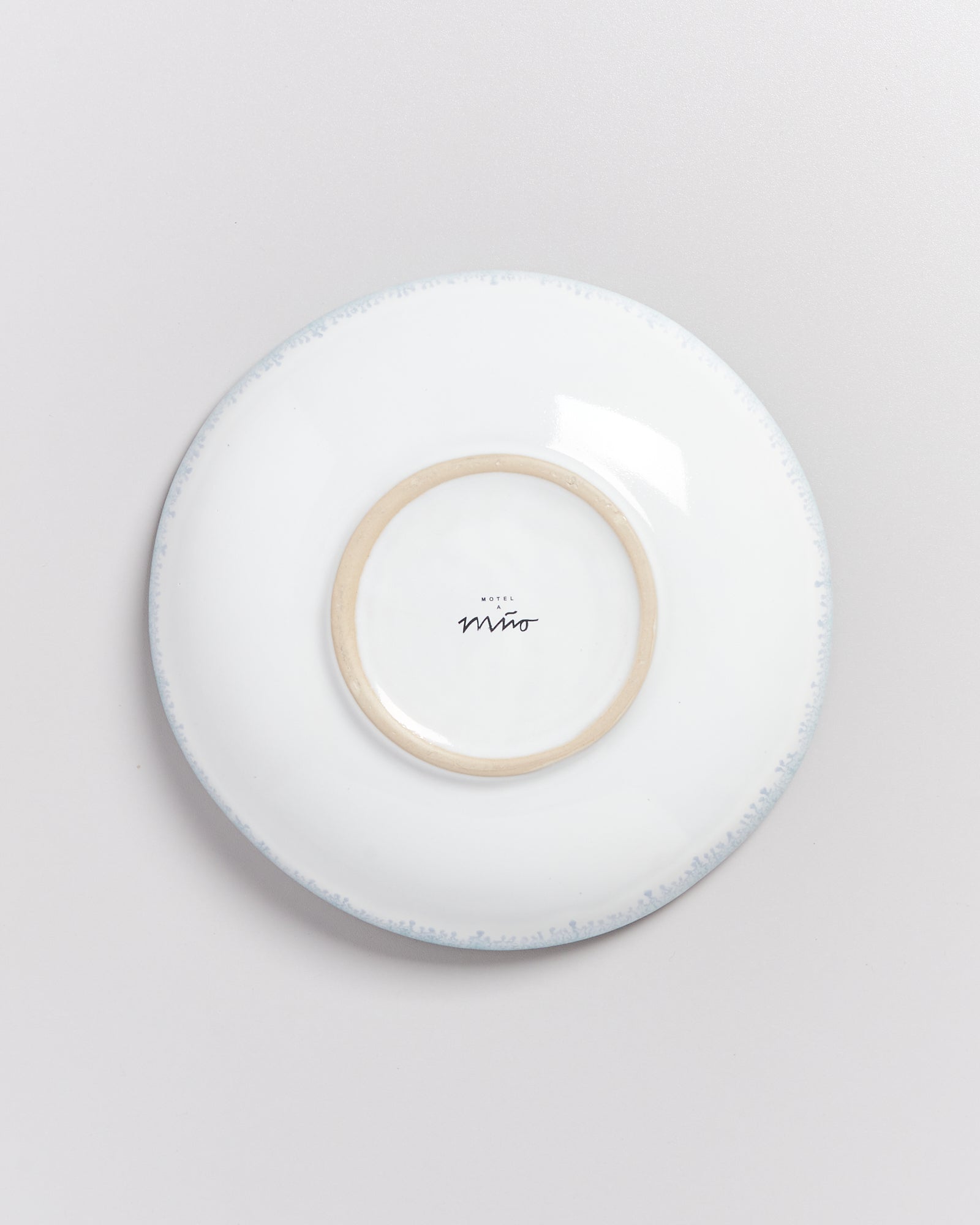 Unterseite eines weißen Tellers mit braunem Rand und Aufschrift auf hellem Hintergrund.