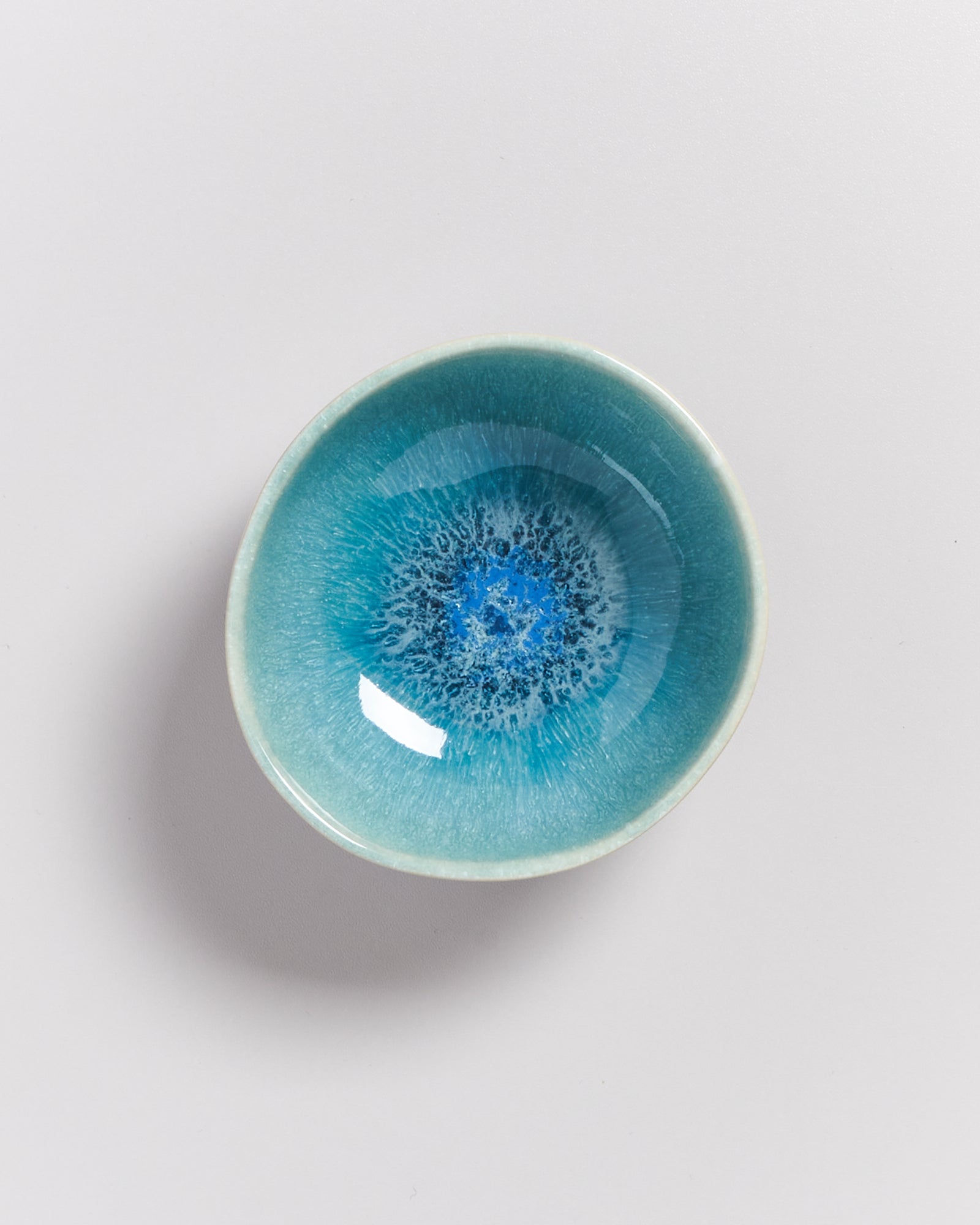 Kleine, runde, blaue Schale mit kunstvoll bemaltem, abstraktem Muster auf weißem Hintergrund.