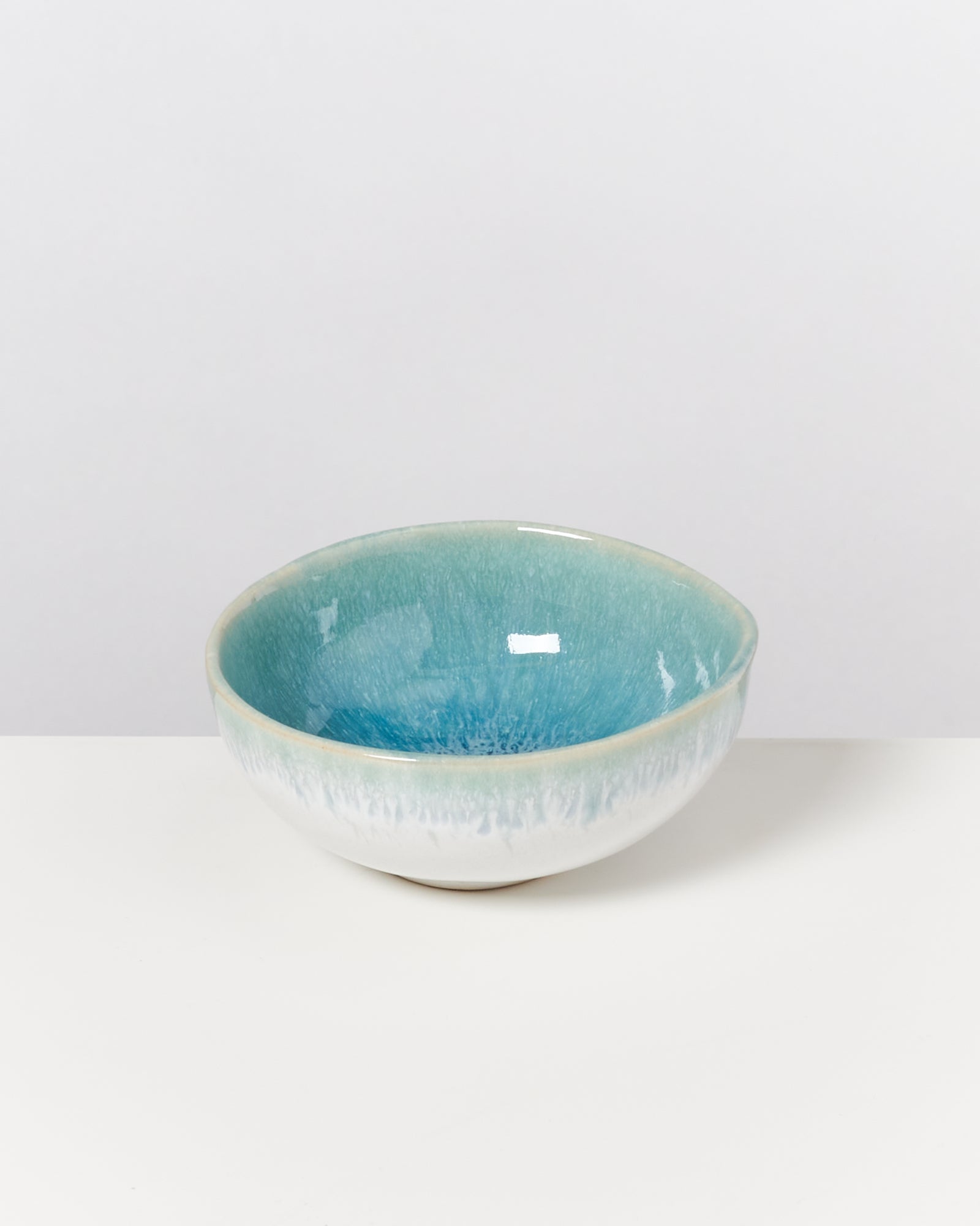 Keramikschale mit blau-grüner Glasur auf hellem Hintergrund.