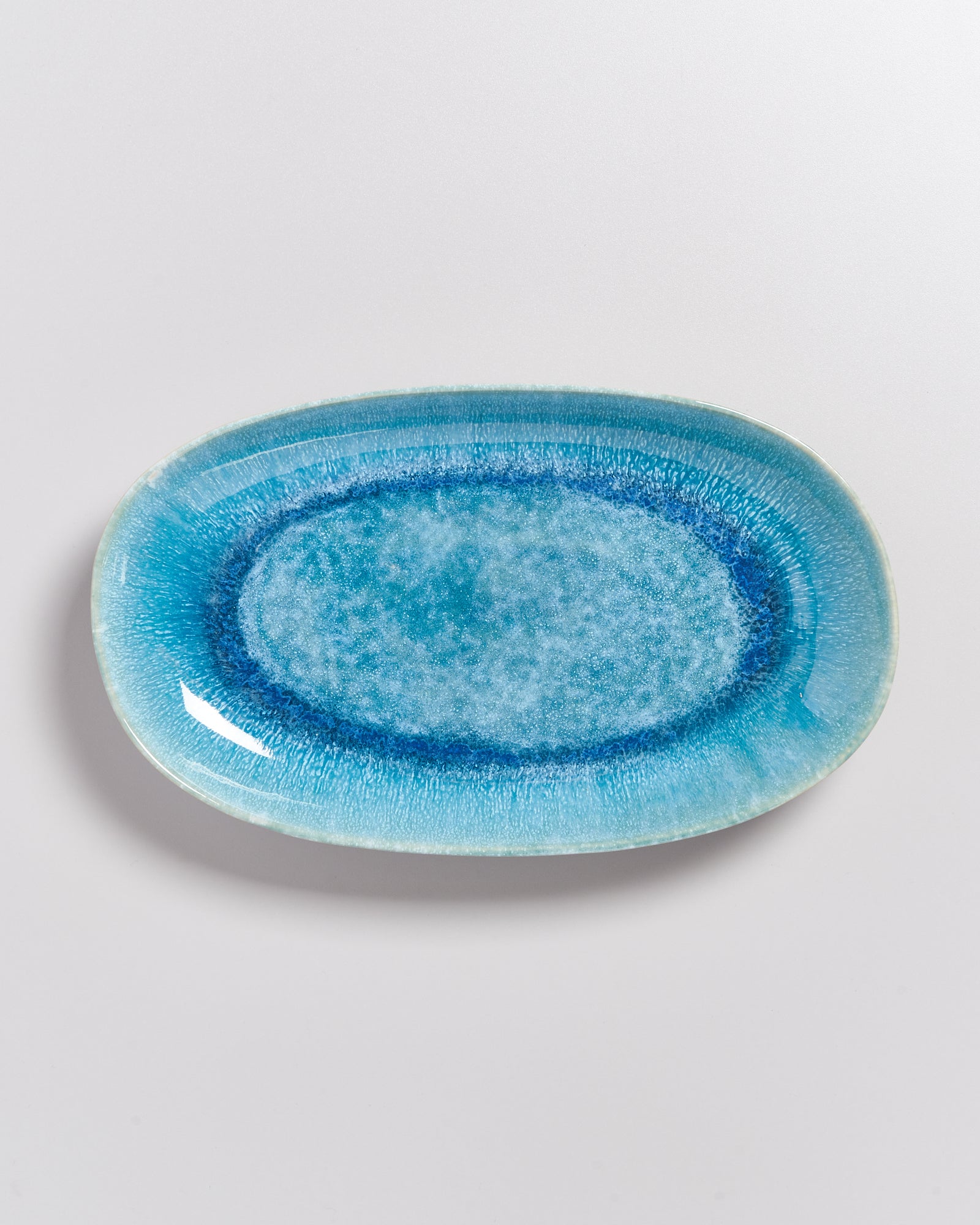 Ovale, hellblaue Keramikplatte mit einem dunkelblauen Randmuster auf weißem Hintergrund.