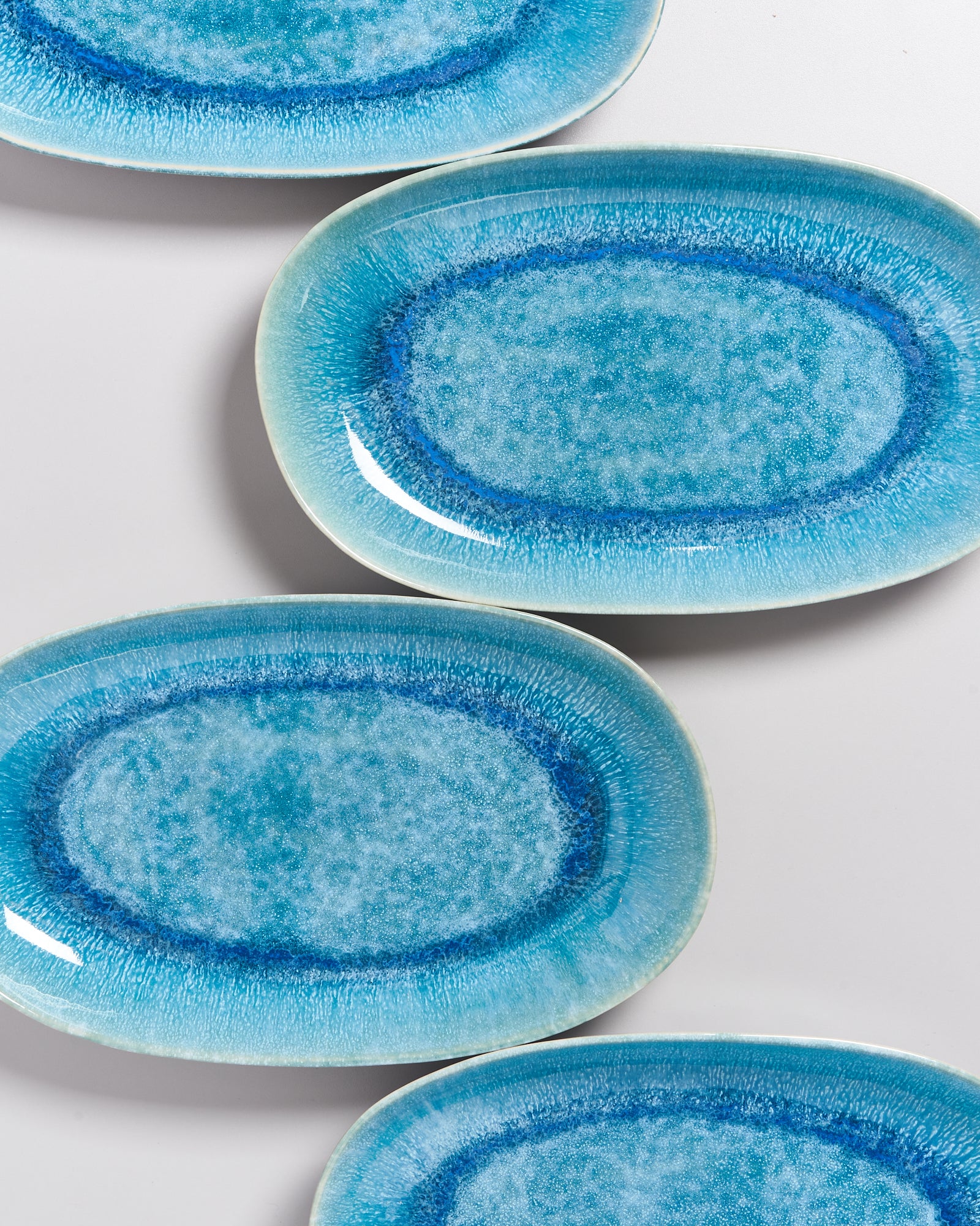 Vier ovale, blaue Teller mit einem aquarellähnlichen Design liegen auf einer weißen Oberfläche.