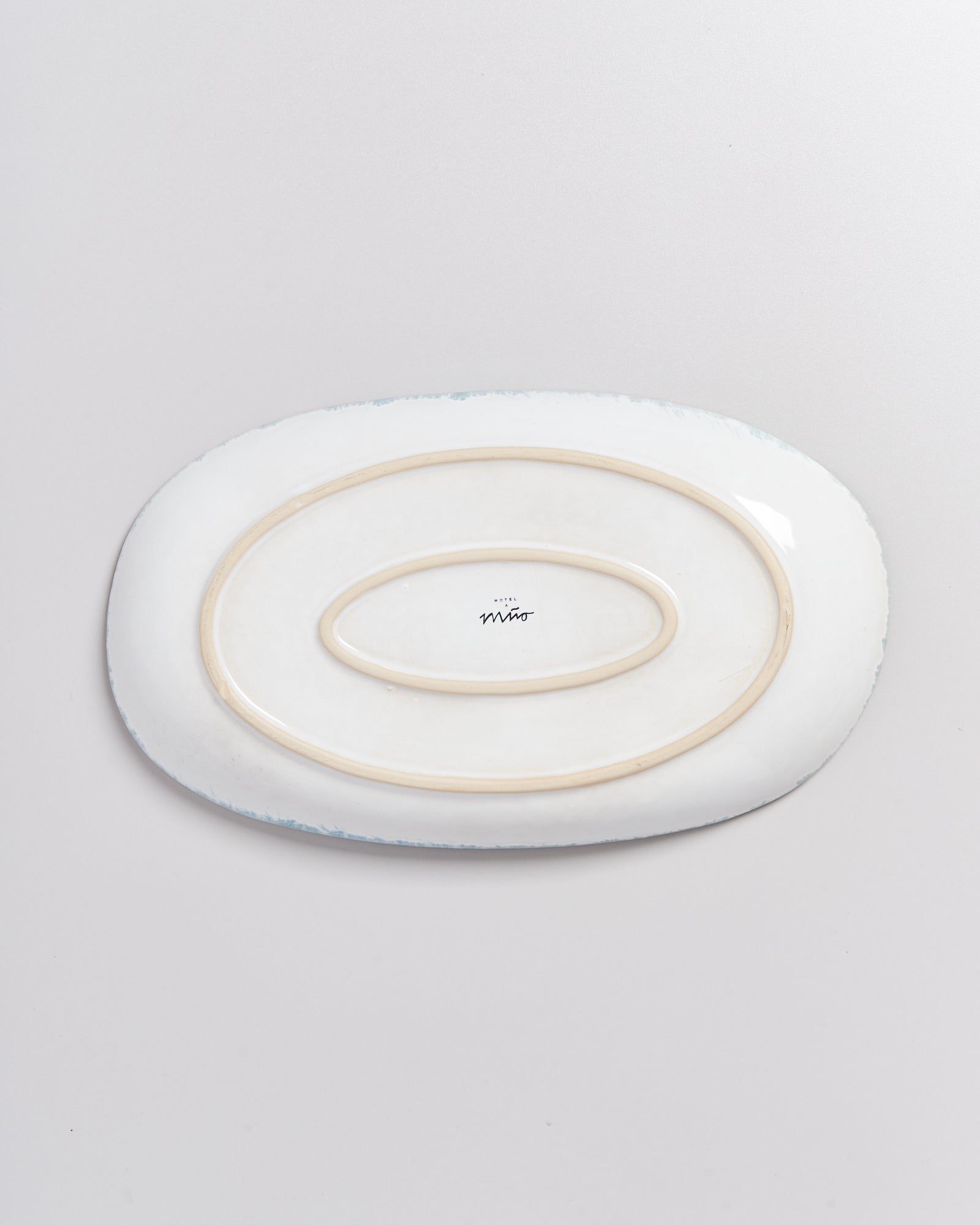 Keramikplatte mit ovalen Rillen auf der Unterseite, auf einer weißen Oberfläche liegend.