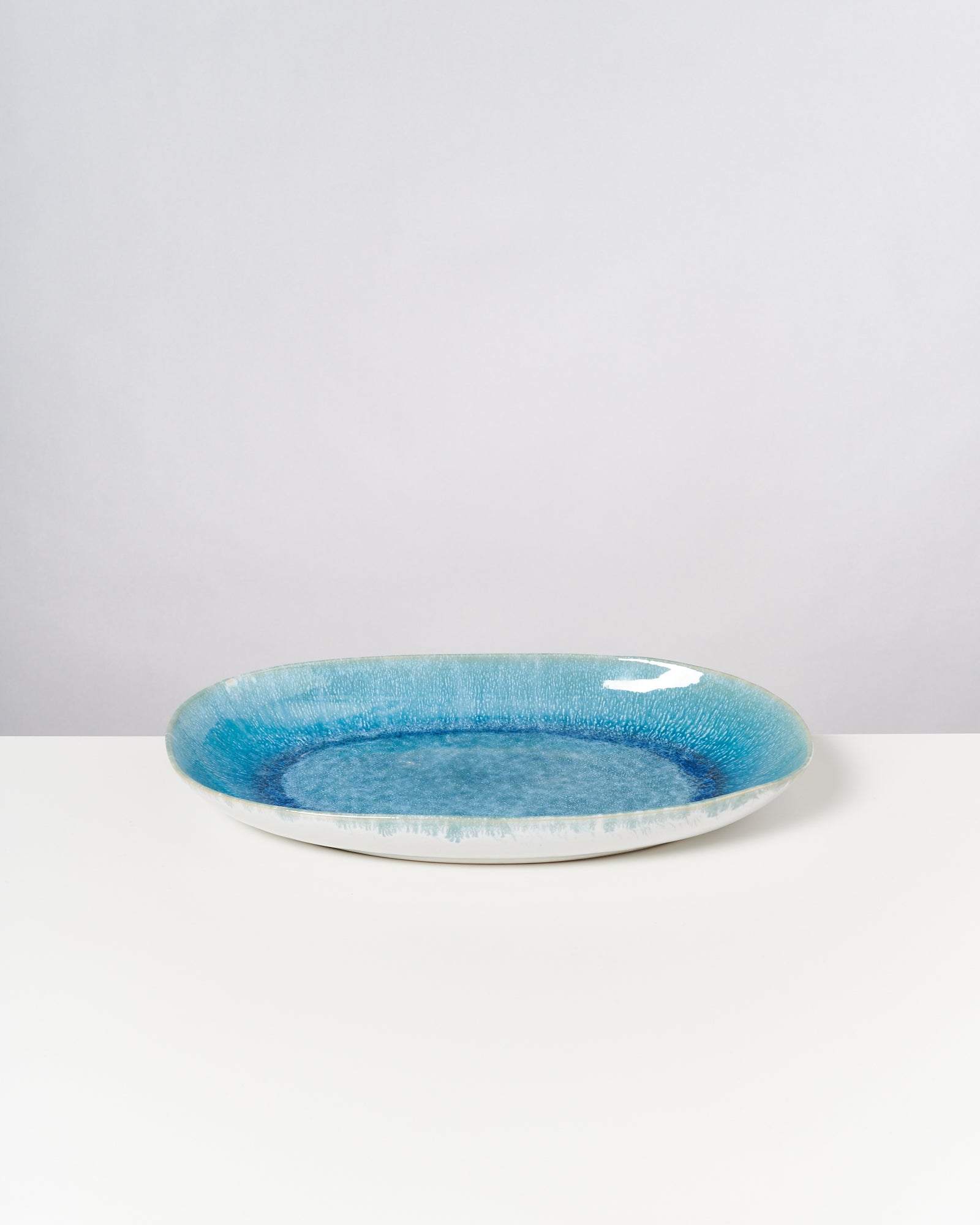 Ein flacher, runder Teller mit einem blauen, strukturierten Muster auf einer weißen Oberfläche.