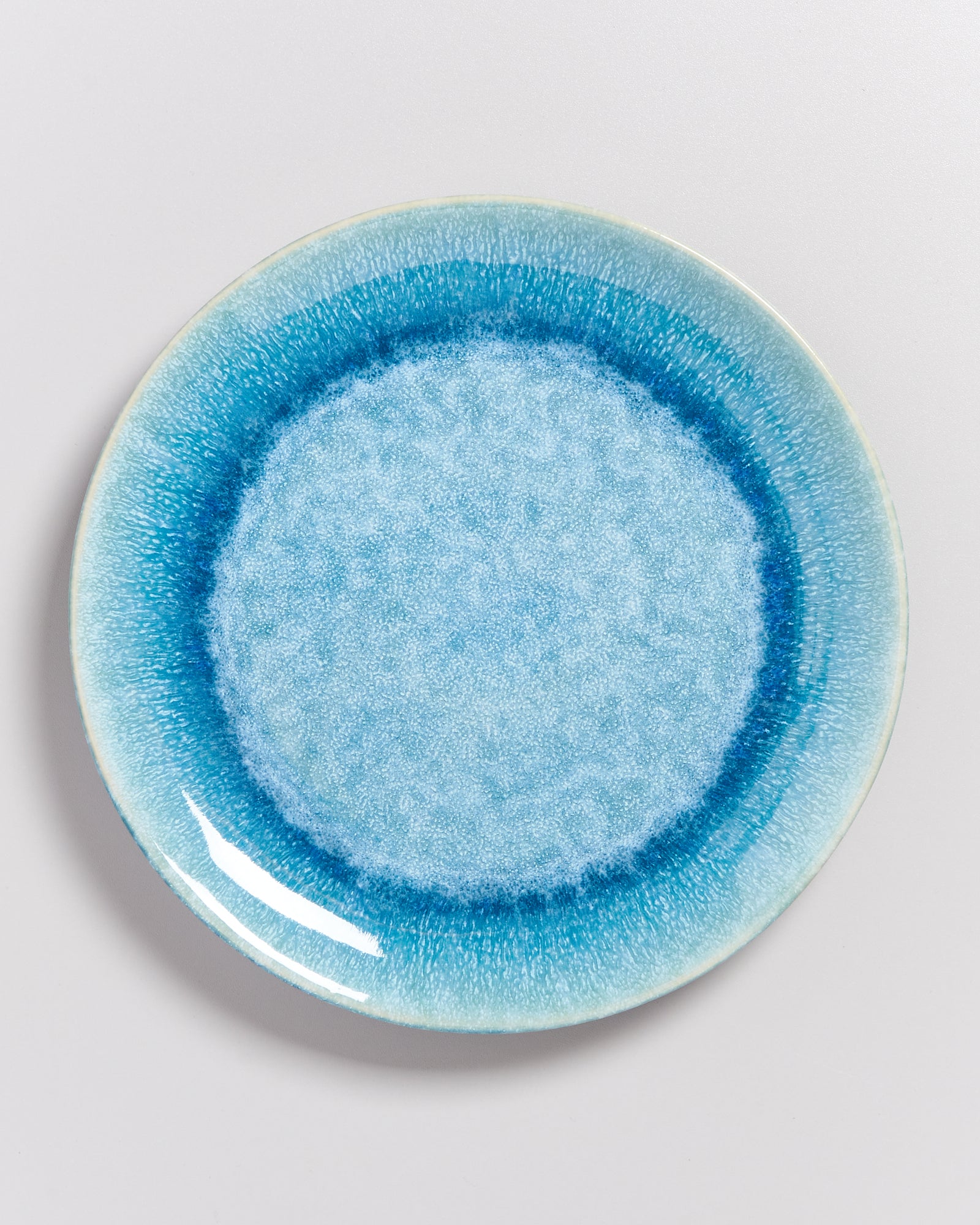 Ein Teller mit einem blauen, texturierten Muster und einem dunkleren blauen Rand auf einer weißen Oberfläche.