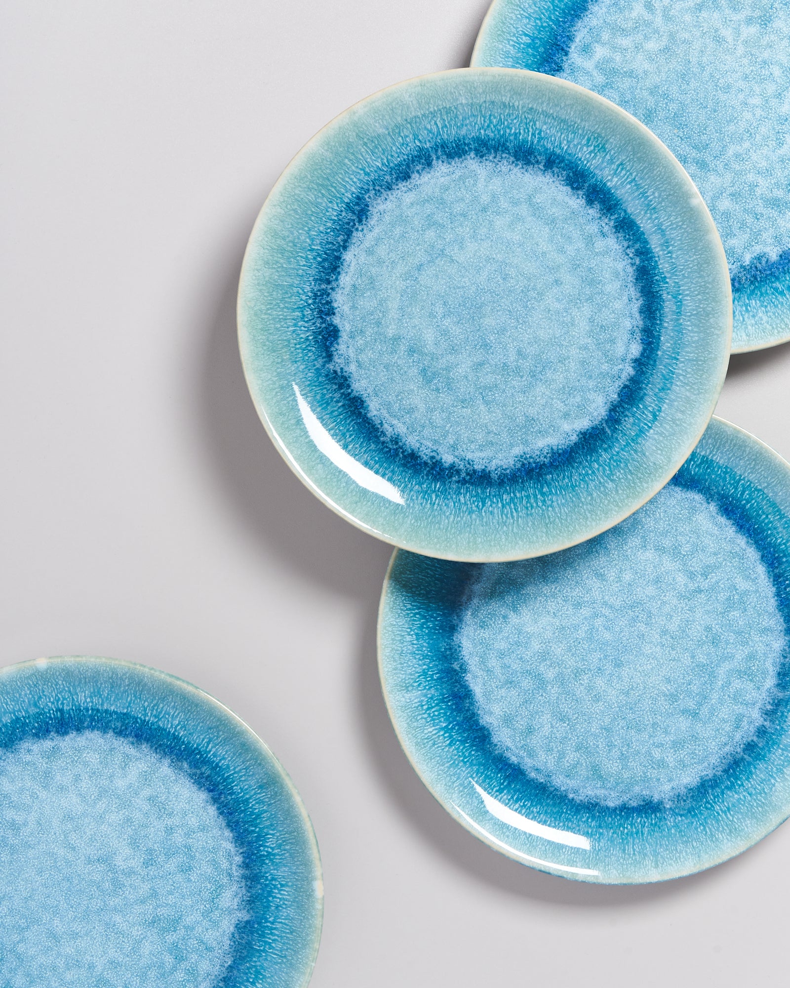 Drei blaue Teller mit dunklem Rand liegen teilweise übereinander auf einem hellen Hintergrund.