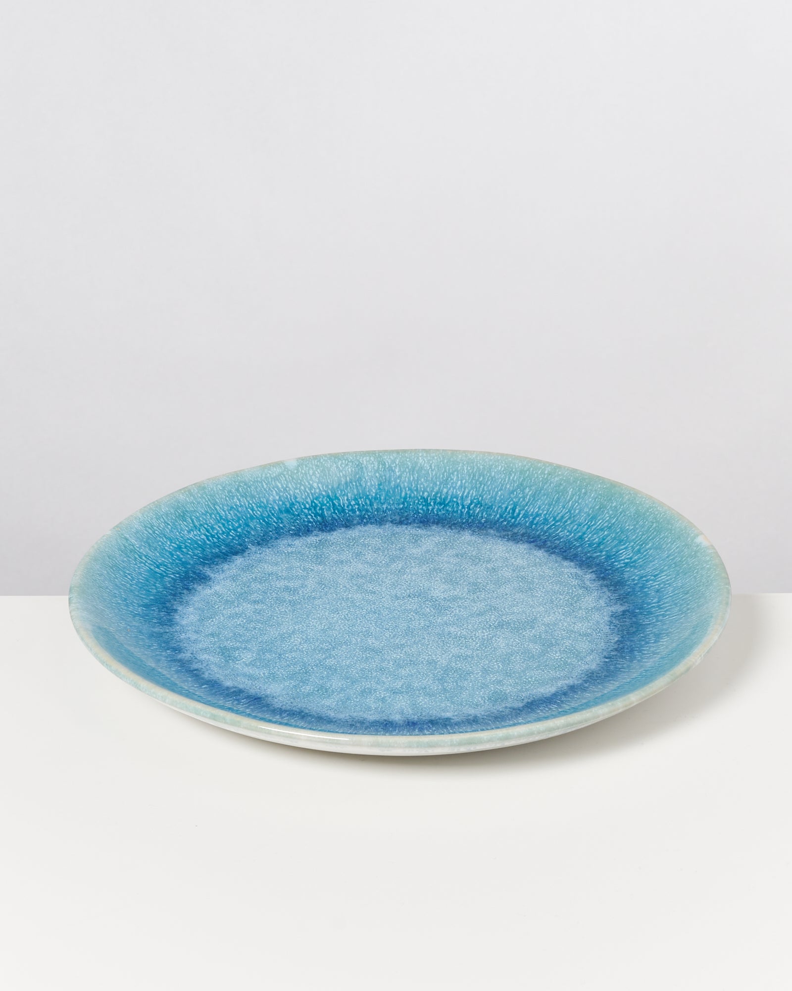 Ein blau schattierter Keramikteller mit glatter Oberfläche liegt auf einem weißen Hintergrund.