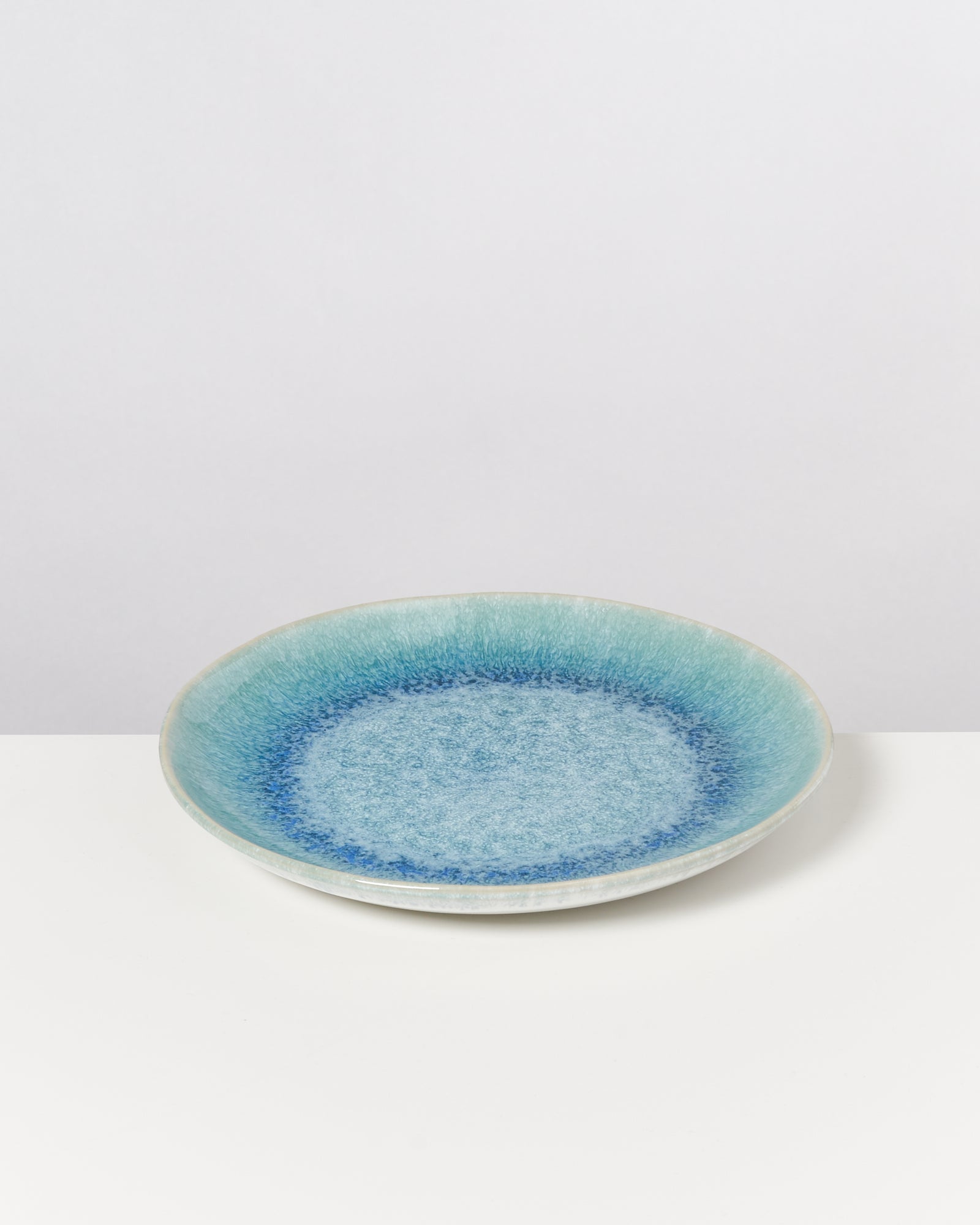 Blauer Keramikteller mit leichtem Farbverlauf von Türkis zu Blau auf weißem Hintergrund.
