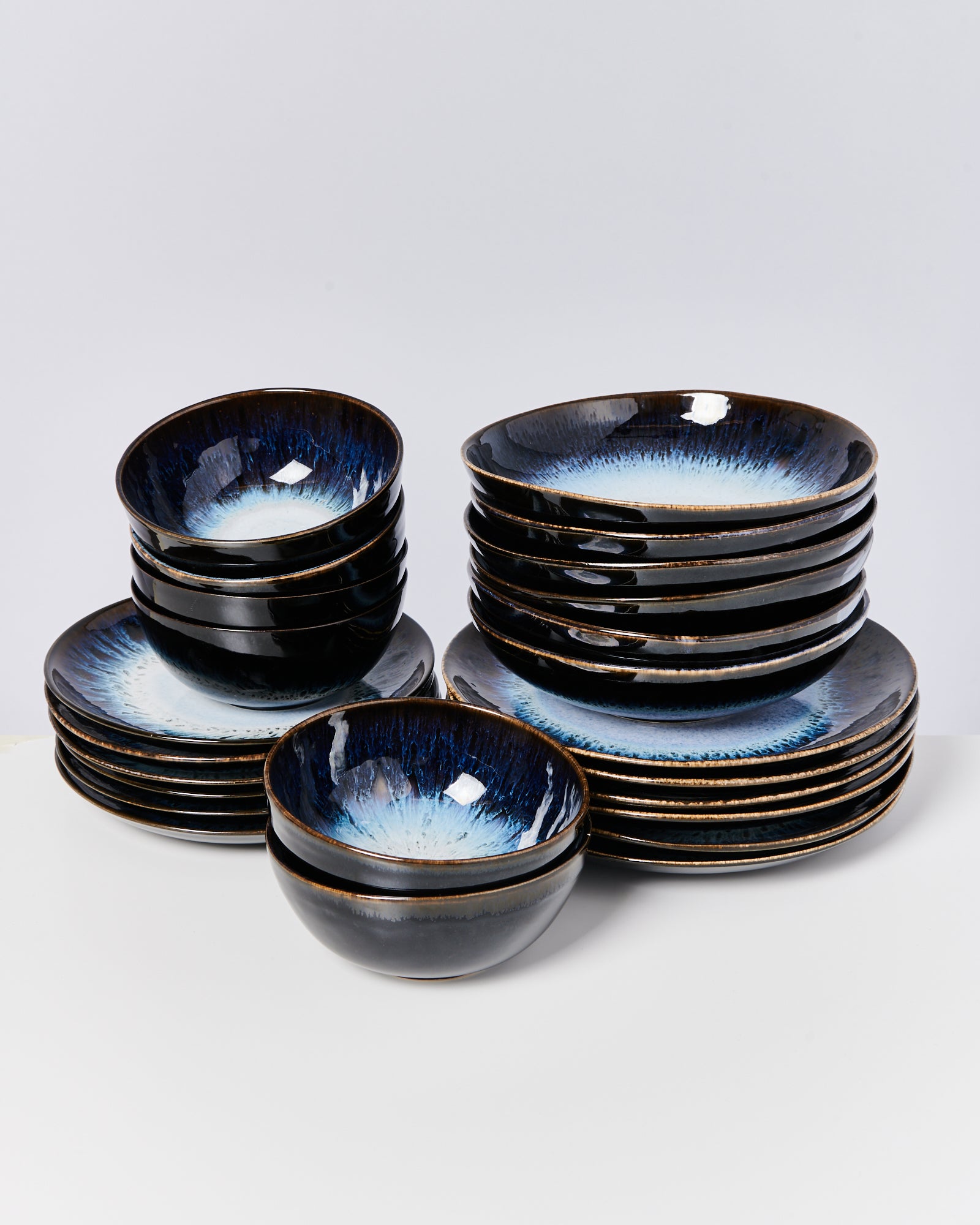 Ein Set aus schwarzen und blauen glänzenden Schalen und Tellern steht gestapelt auf einem weißen Untergrund.