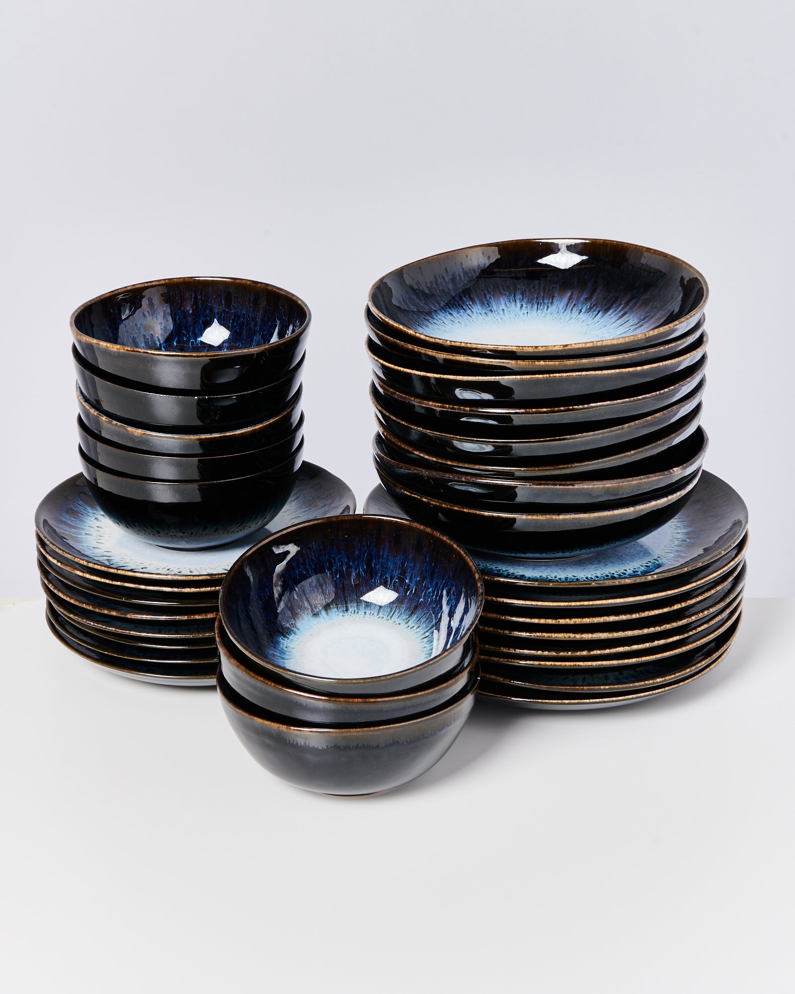 Ein Stapel aus schwarzem Keramikgeschirr mit blauer Innenglasur steht auf einem weißen Hintergrund.