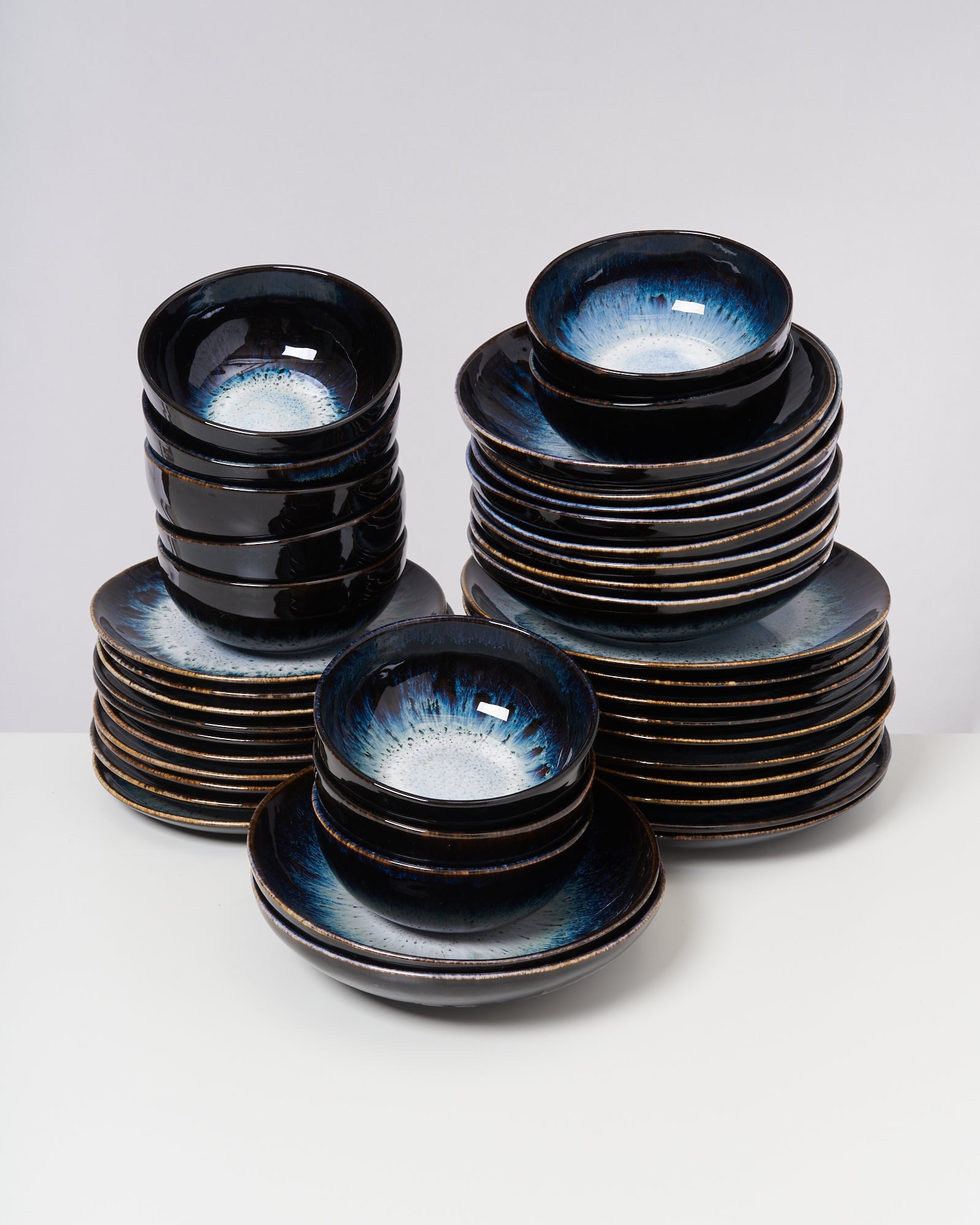 Stapel aus schwarzen, glänzenden Keramikschüsseln und Tellern mit blauen Akzenten auf einem weißen Tisch.