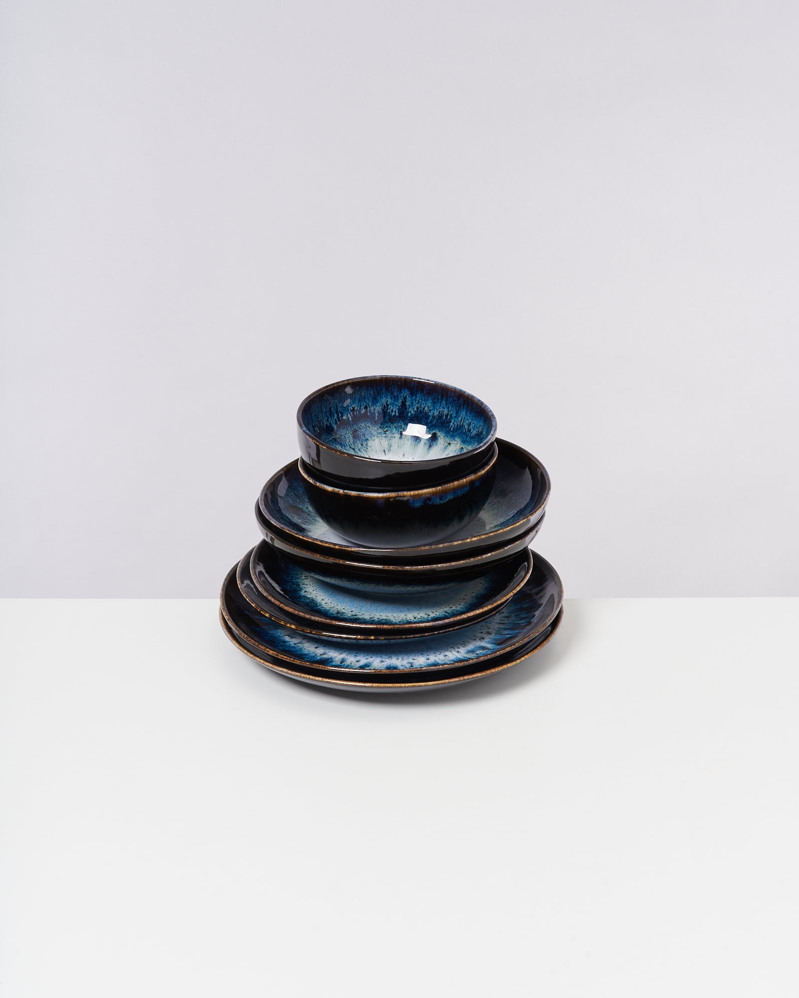 Ein Stapel dunkelblau marmorierter Keramikschalen auf einem weißen Tisch vor einem grauen Hintergrund.