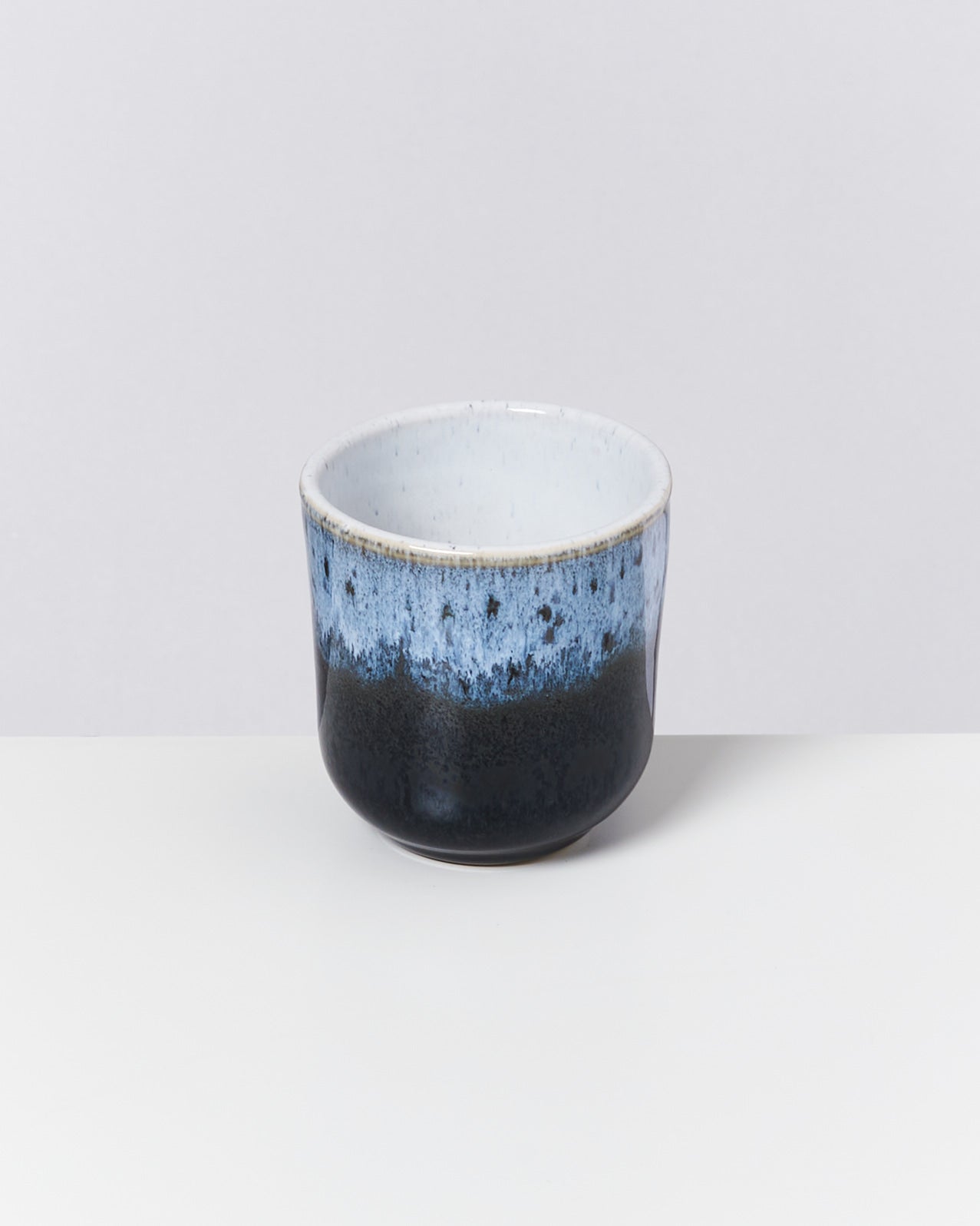 Keramikbecher mit blau-schwarzer Glasur auf hellem Hintergrund.