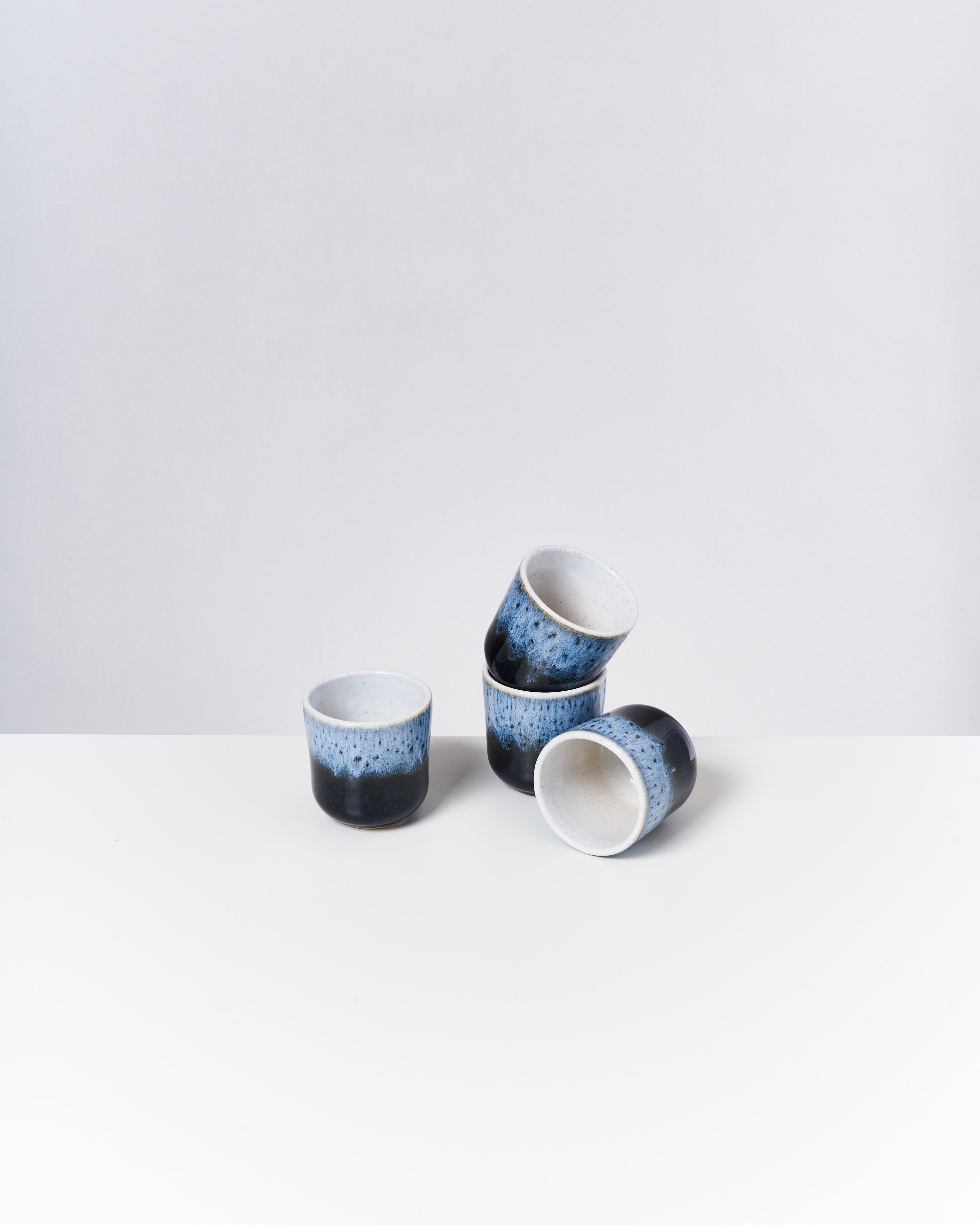 Vier blau-schwarz glasierte Keramiktassen stehen auf einem weißen Tisch.