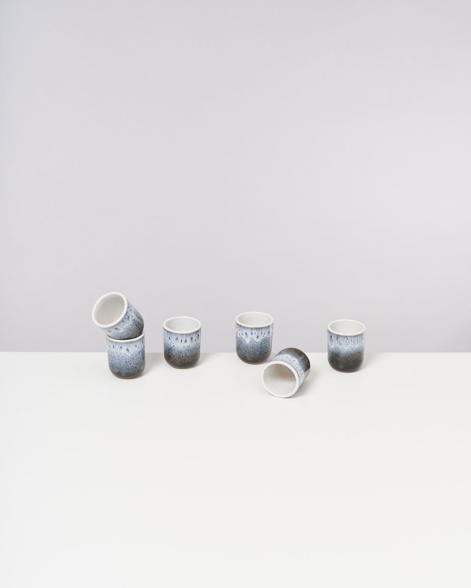 Sechs blaue Keramikbecher auf weißem Tisch, einer liegt auf der Seite.
