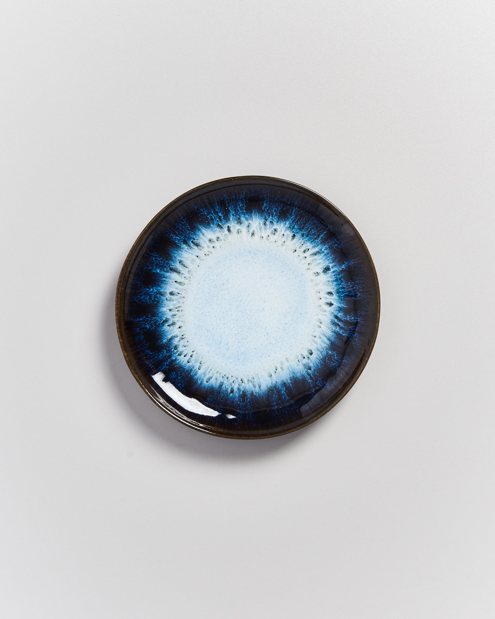 Runde Keramikschale mit einem blauen, radialen Muster auf weißem Hintergrund.