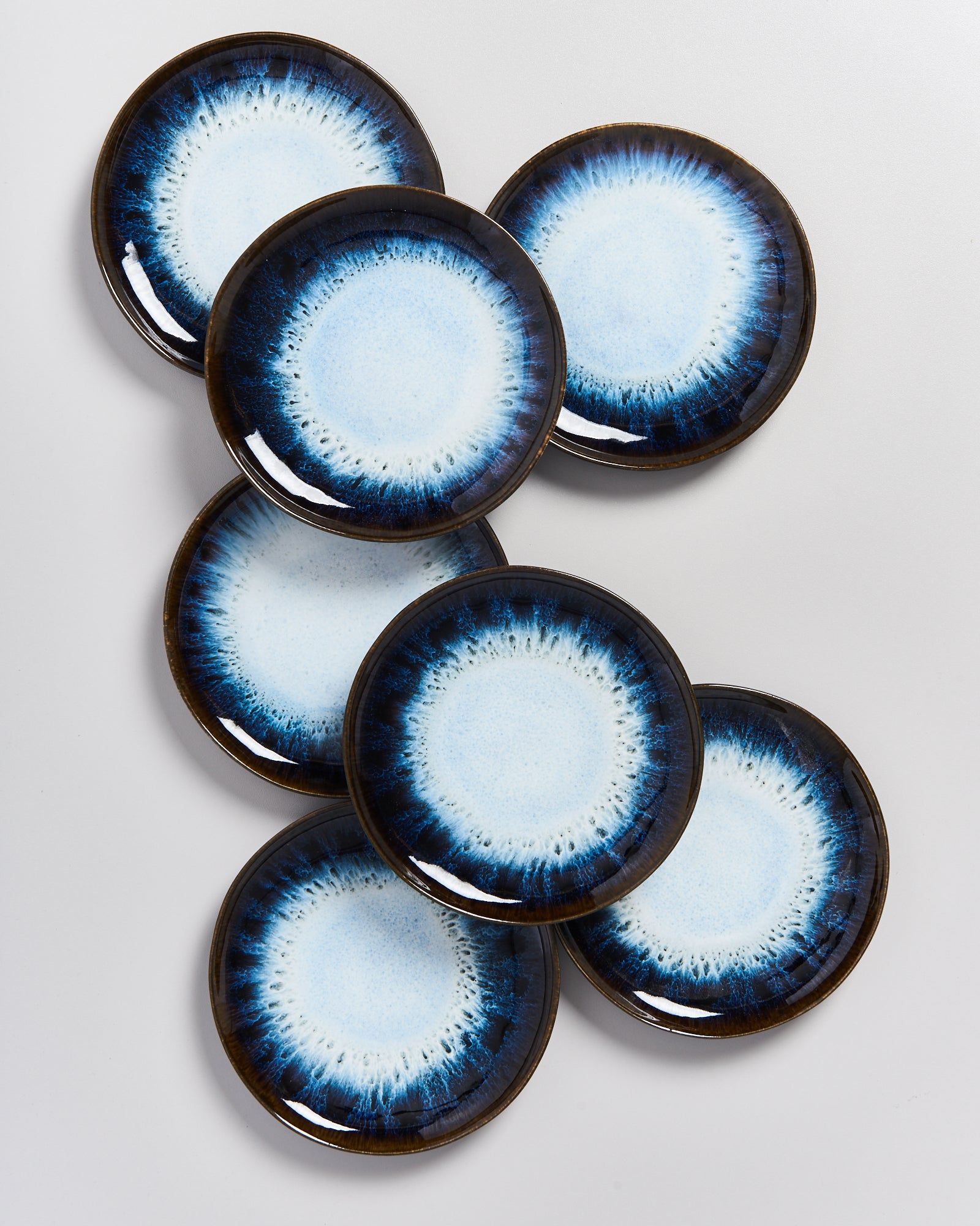 Sieben runde Teller mit blauem und weißem Muster liegen überlappend auf einer hellen Oberfläche.