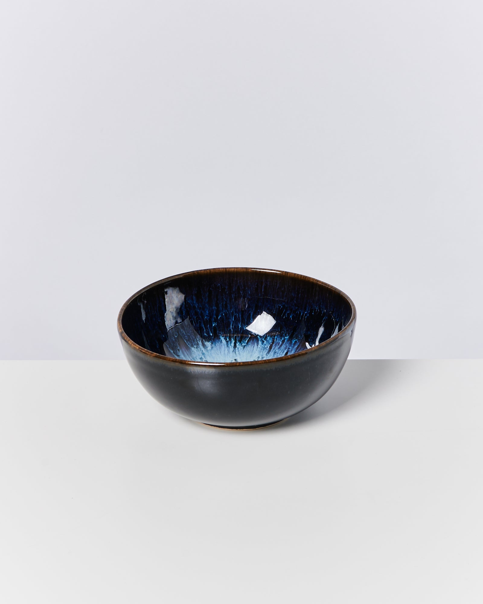 Schwarze Keramikschale mit blauem Inneren steht auf einem weißen Untergrund.