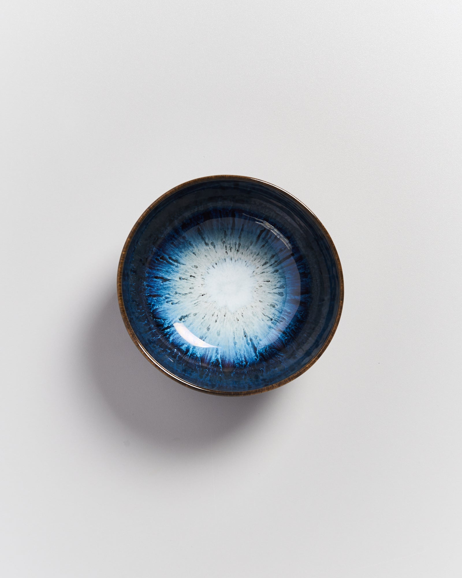 Eine kleine, runde Schale mit blauer Glasur und weißem Zentrum auf weißem Hintergrund.