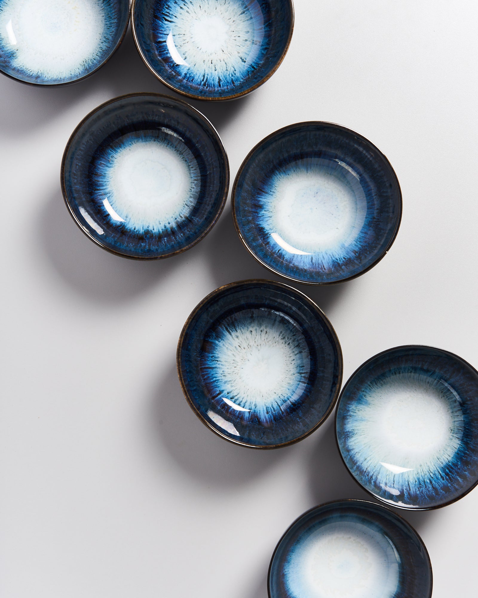 Sieben blau-weiße Schalen mit radialem Muster liegen auf einer hellen Oberfläche.