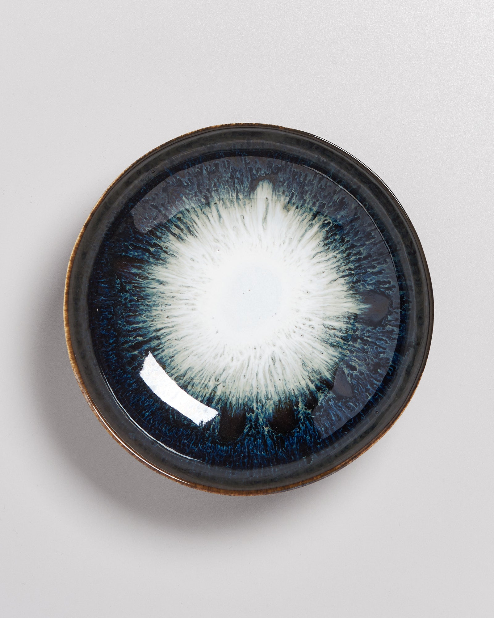 Keramikschale mit blau-weißem, augenähnlichem Muster auf einem hellen Hintergrund.