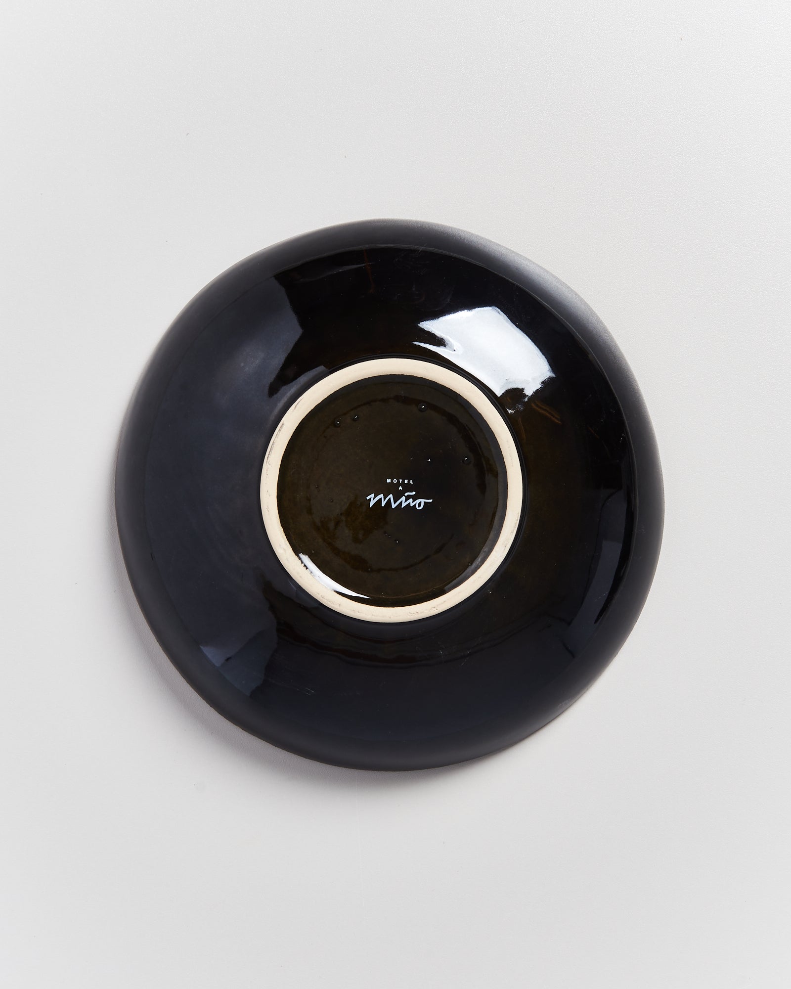 Schwarzer Teller auf der Rückseite liegend mit weißem Rand und kleinem Logo in der Mitte auf hellem Hintergrund.