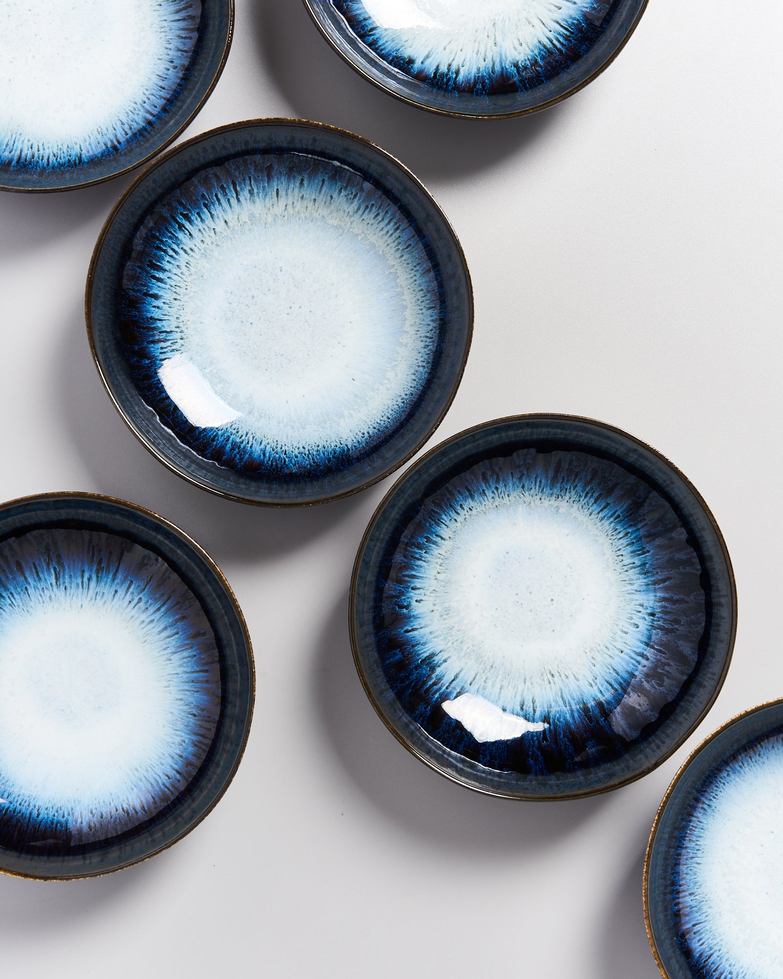 Sechs blaue Teller mit radialem Muster auf weißem Hintergrund.