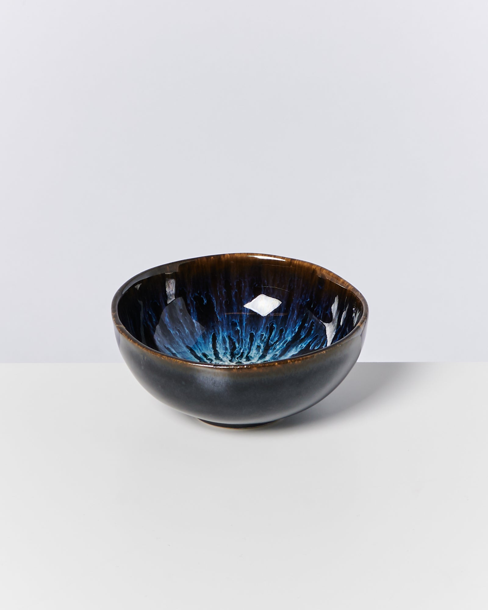 Schüssel mit glänzendem, blauem und braunem Muster auf hellem Hintergrund.