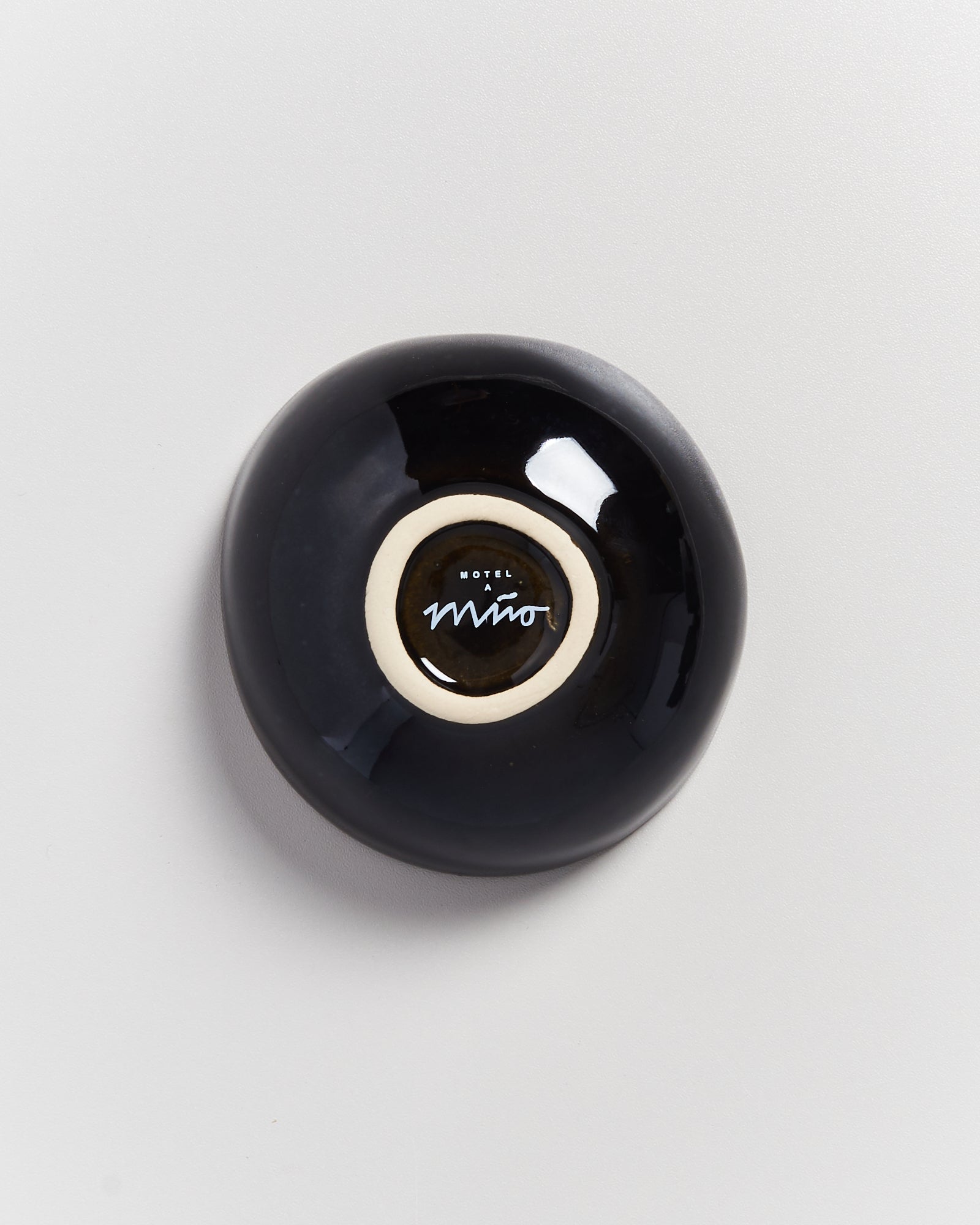 Schwarzer Keramikgegenstand mit cremefarbenem Rand und der Aufschrift "Motel Mió" in der Mitte, auf weißem Hintergrund.