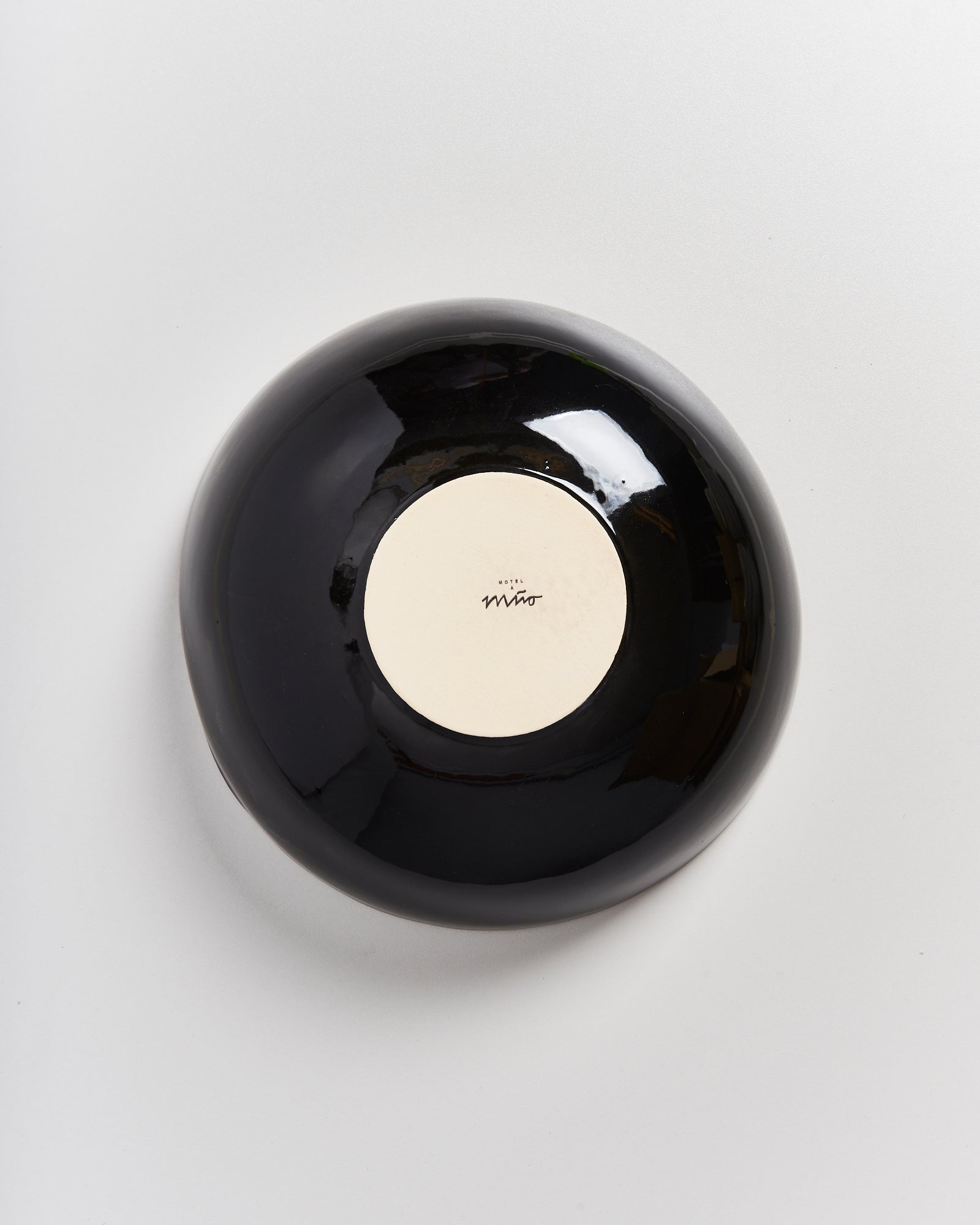 Schwarze glänzende Schale mit beigem Boden und schwarzer Signatur darauf, auf hellgrauem Hintergrund.