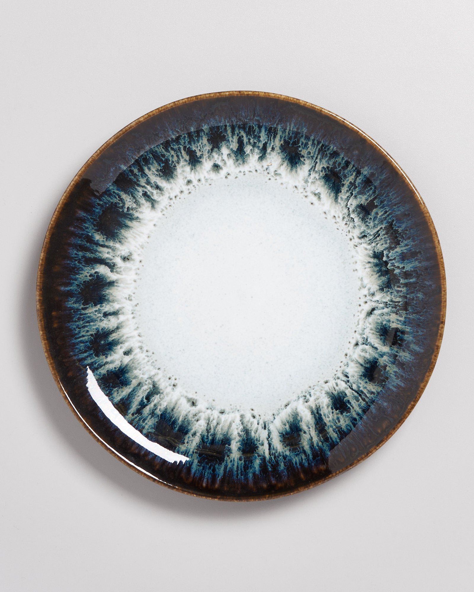 Keramikteller mit blau-weißer glasierter Musterung am Rand auf grauem Hintergrund.